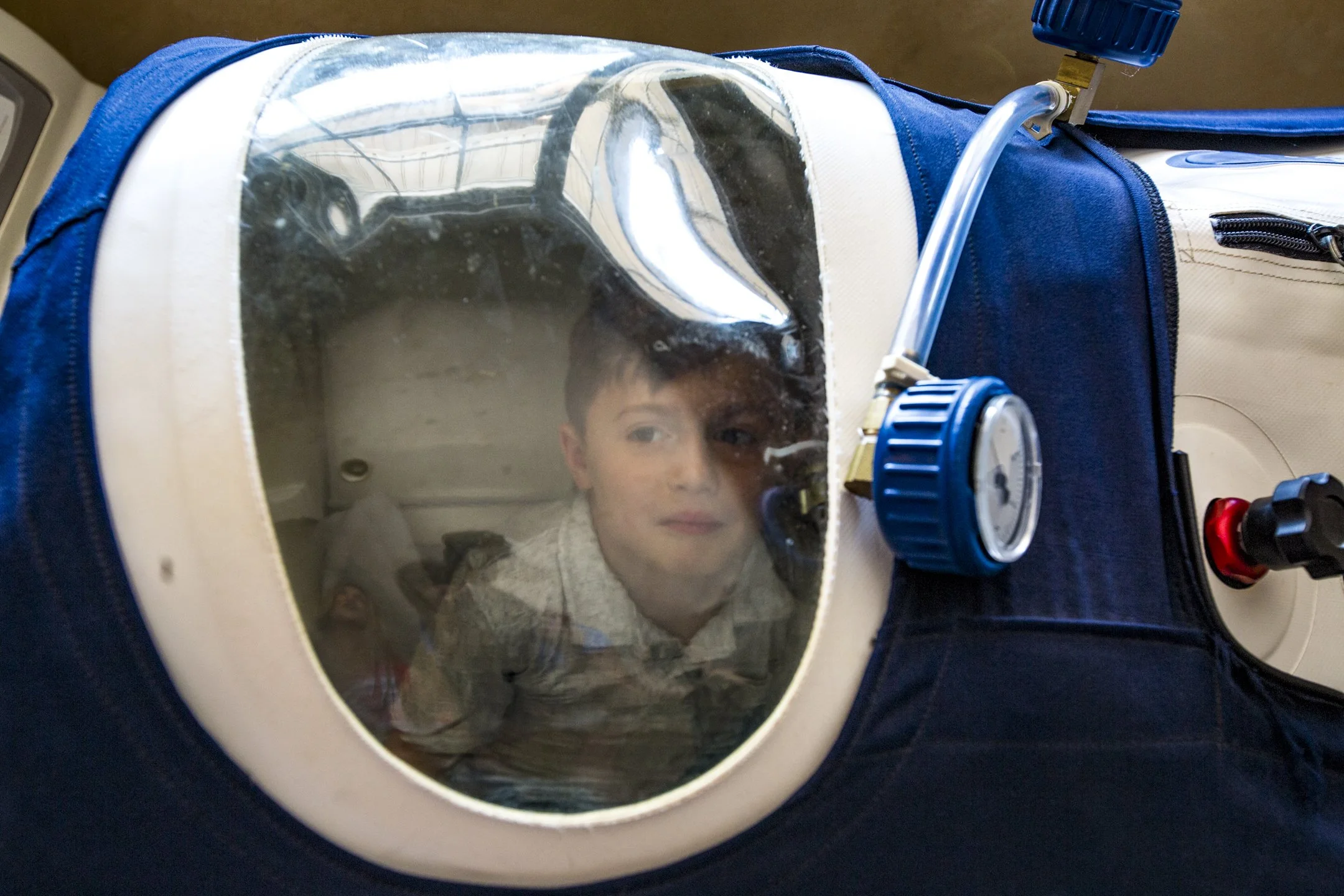 A young boy looking through a clear plastic window on a pet carrier, with a small dog inside.