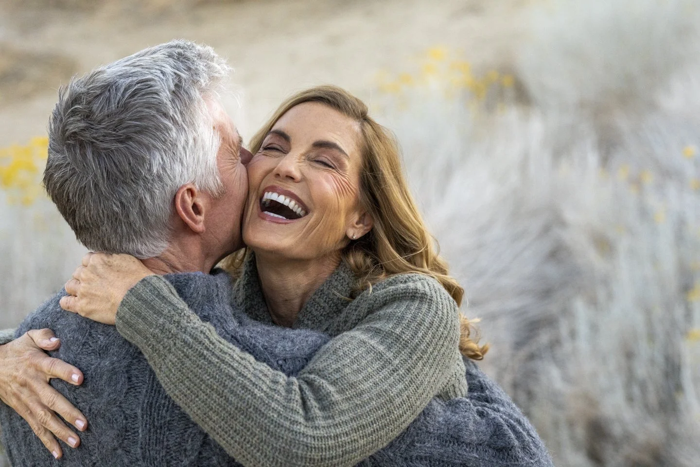 Older man with gray hair hugging a smiling woman with long, wavy hair outdoors.