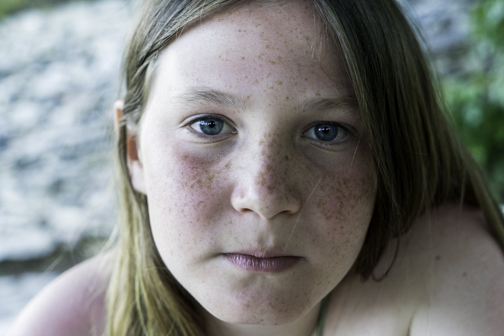 A close-up of a girl with blue eyes and freckles, looking directly at the camera.