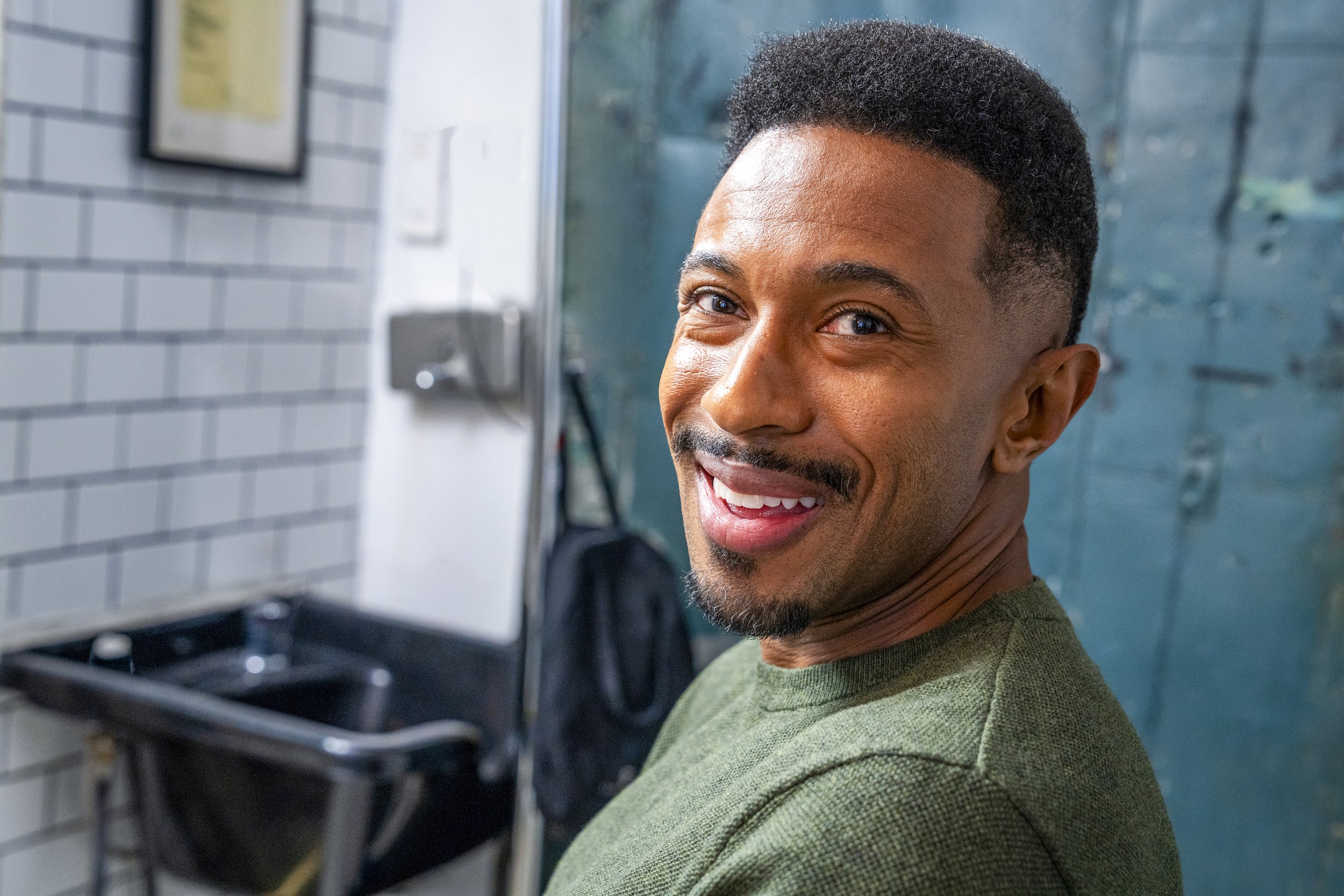 A smiling man with short black hair and a goatee, wearing a green shirt, looking at the camera.