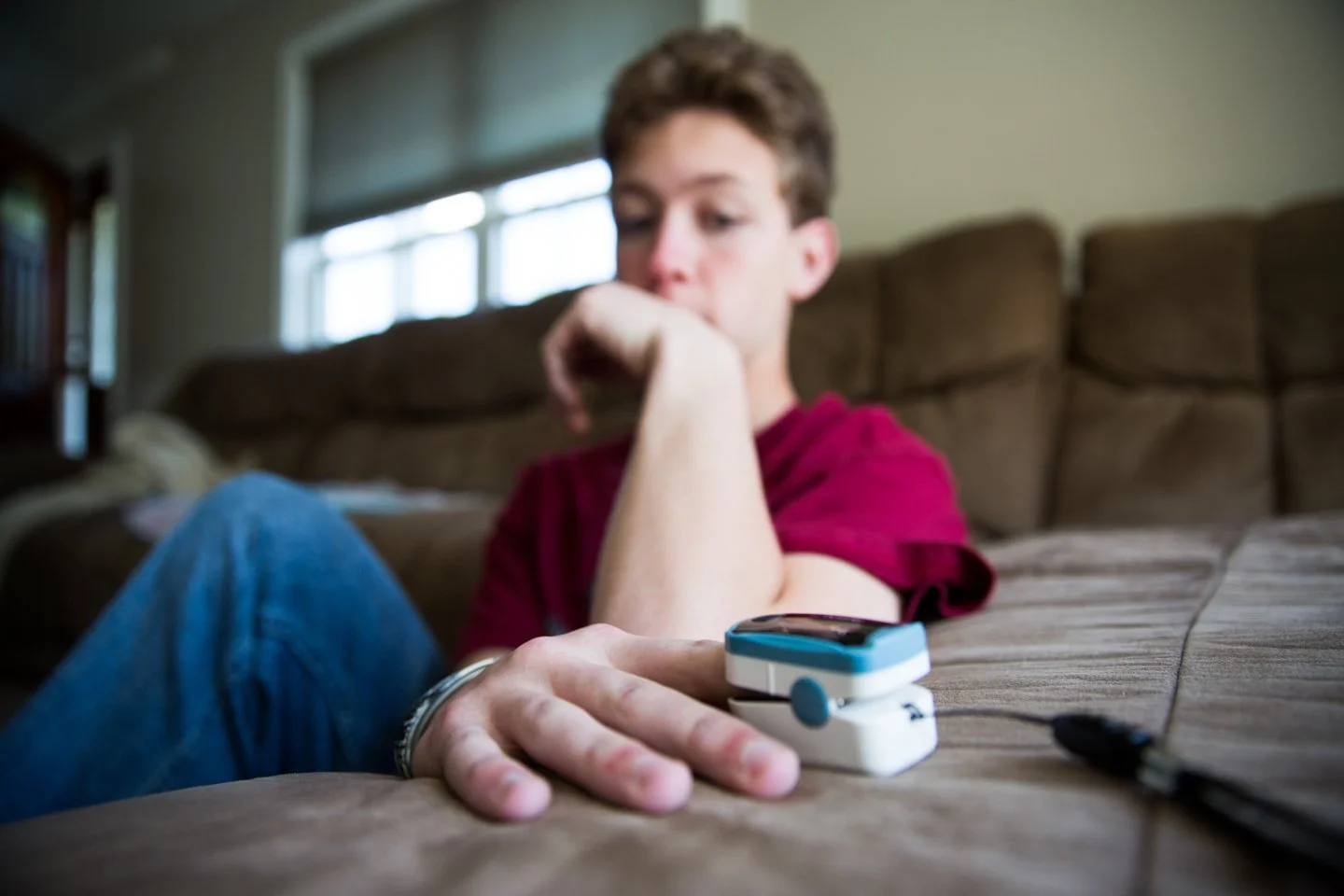 Young person sitting on a couch with an insulin pump attached to their arm, looking down thoughtfully.