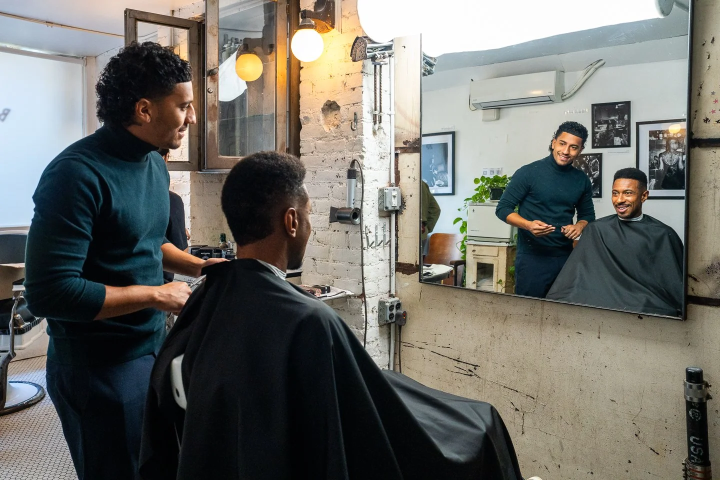 Barber giving a haircut to a customer in a modern barbershop, with a stylist smiling in the mirror.
