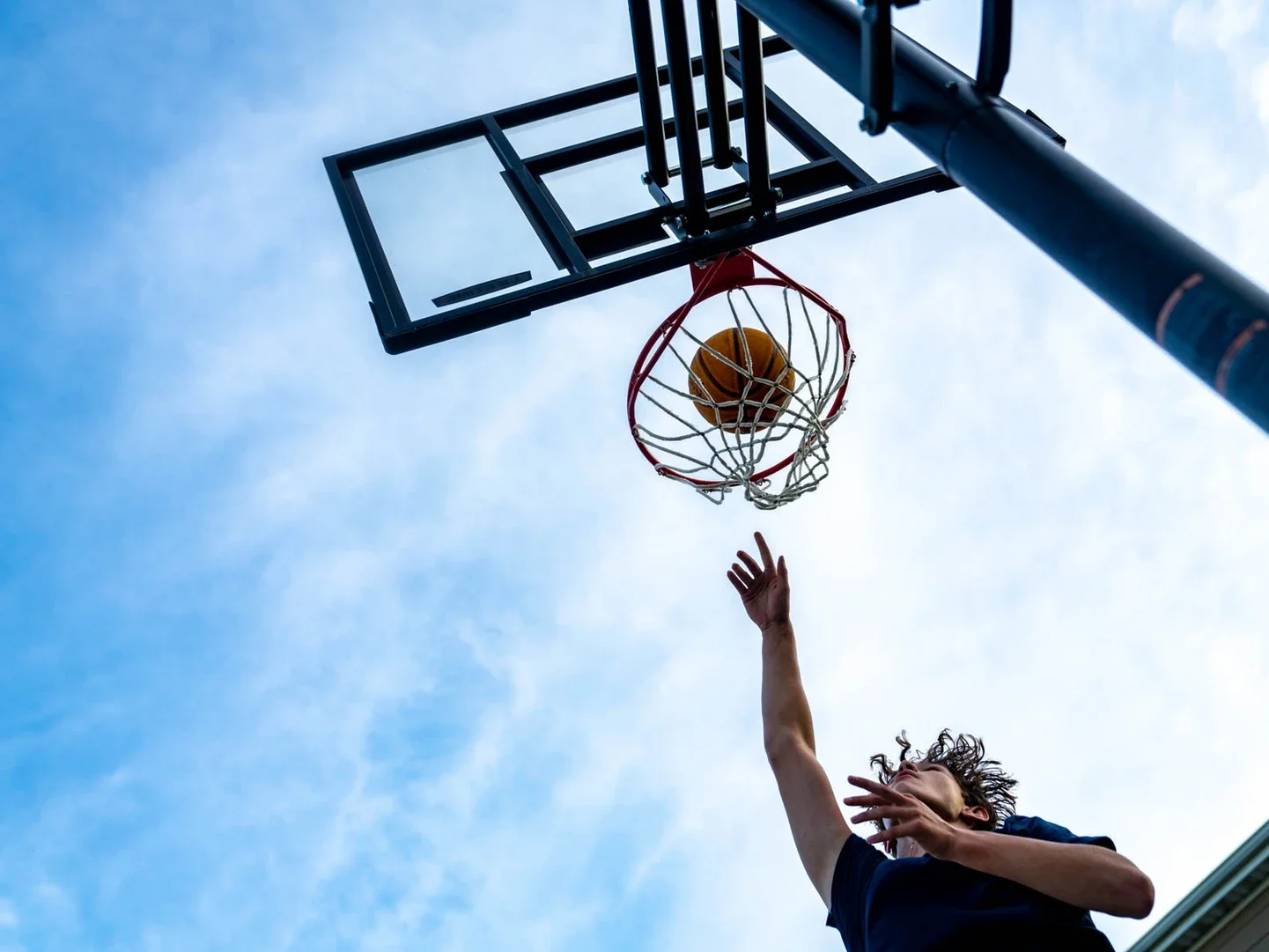A person playing basketball, reaching up to shoot or block the ball towards the hoop on an outdoor court during the day.