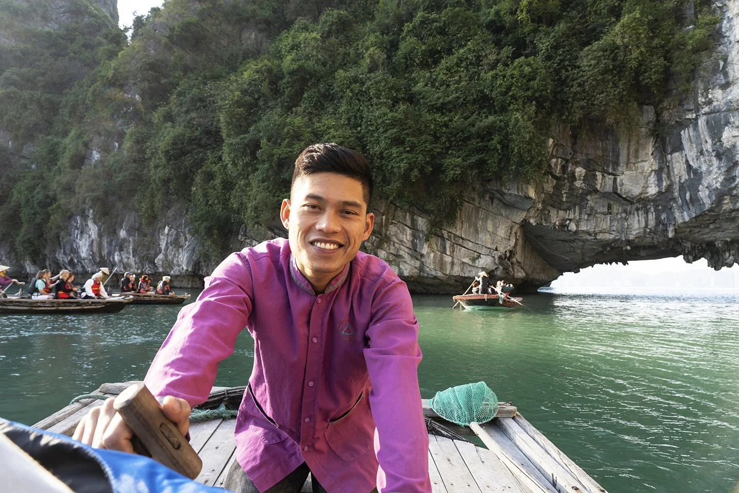 Man on a boat taking a selfie with a large cave and other boats with tourists in the background.