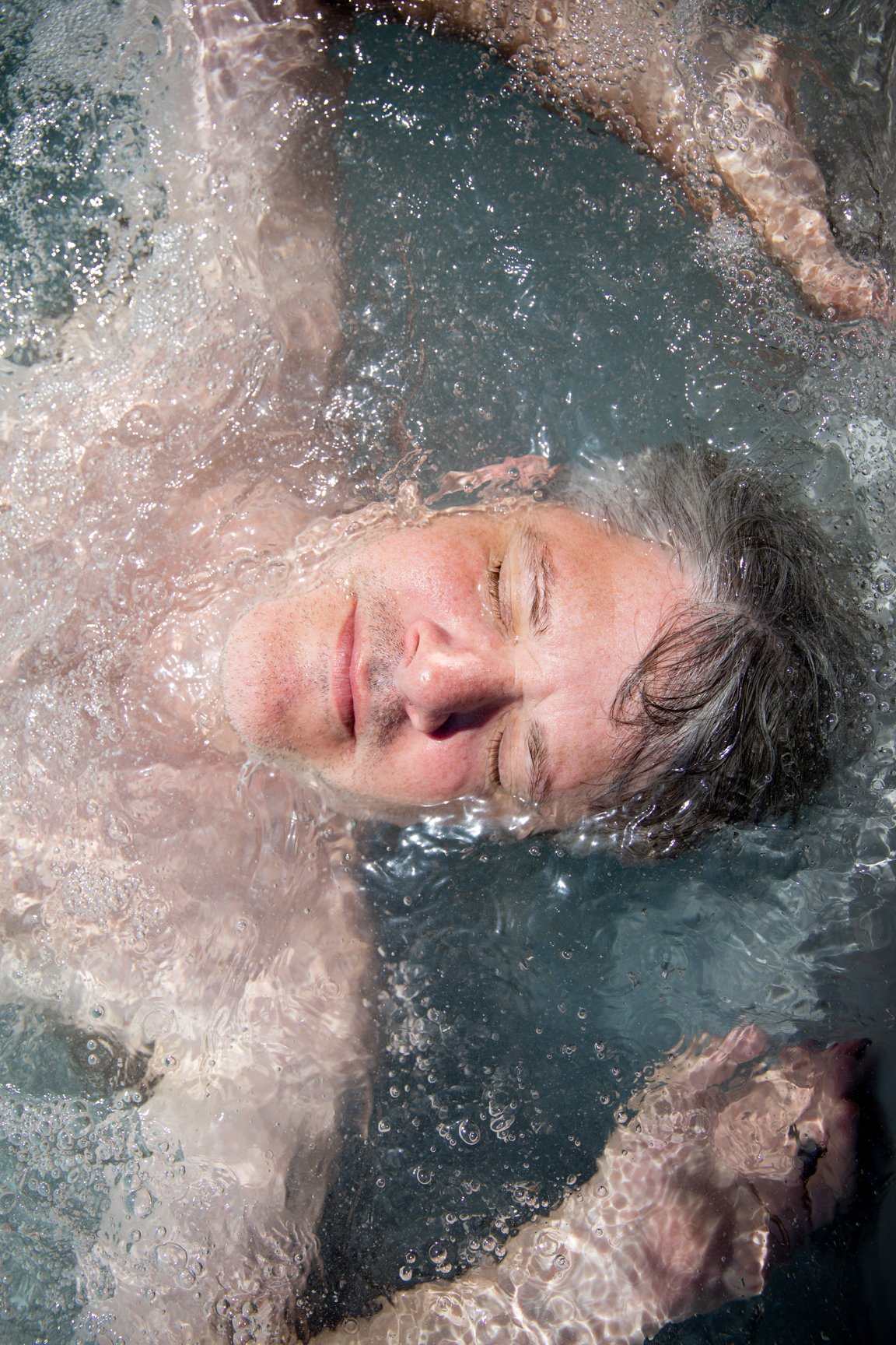 A man with closed eyes is floating in water, appearing relaxed.