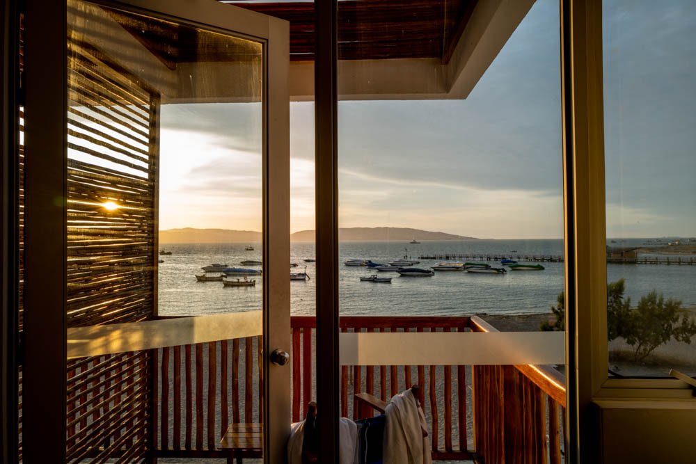 View of a harbor with boats docked, seen from a balcony with wooden railing and a door, during sunset.