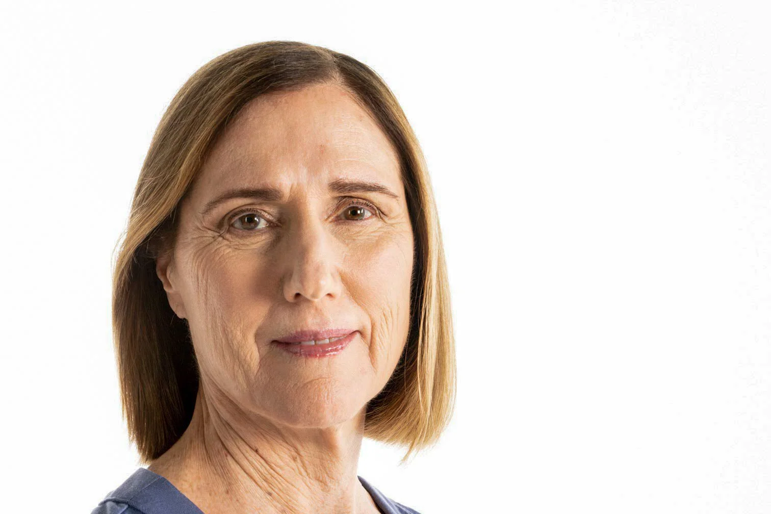 Close-up of a middle-aged woman with shoulder-length light brown hair, wearing a blue top, against a white background.