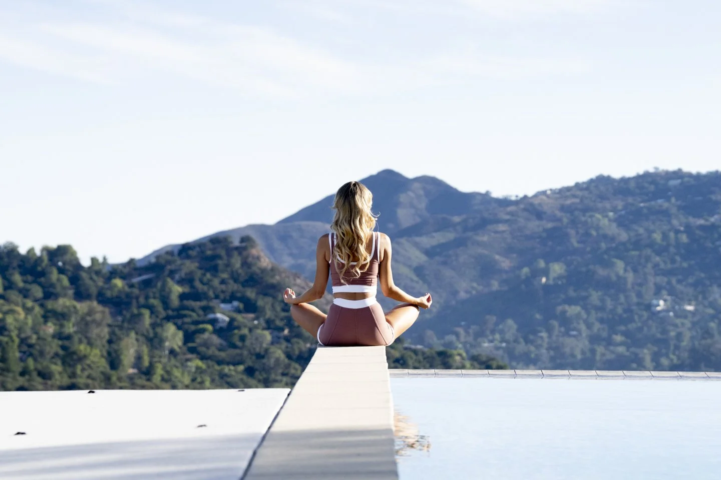 A woman practicing yoga on a dock beside a reflecting pool, with hills in the background.