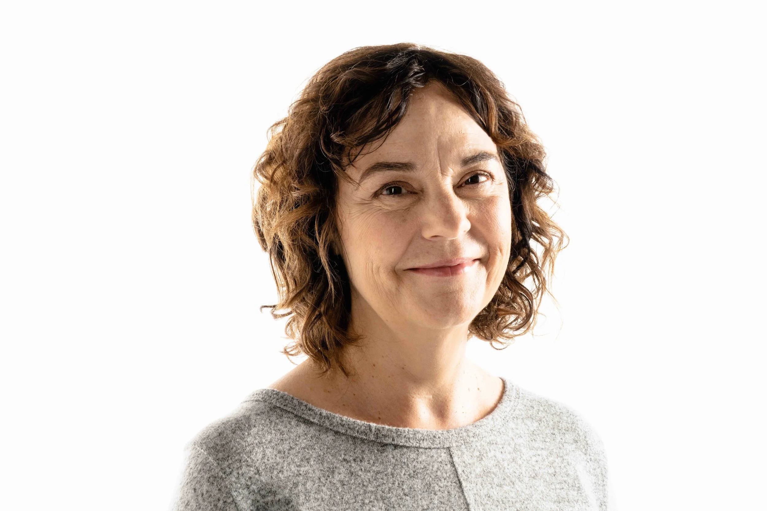 A woman with curly brown hair smiling at the camera against a plain white background.