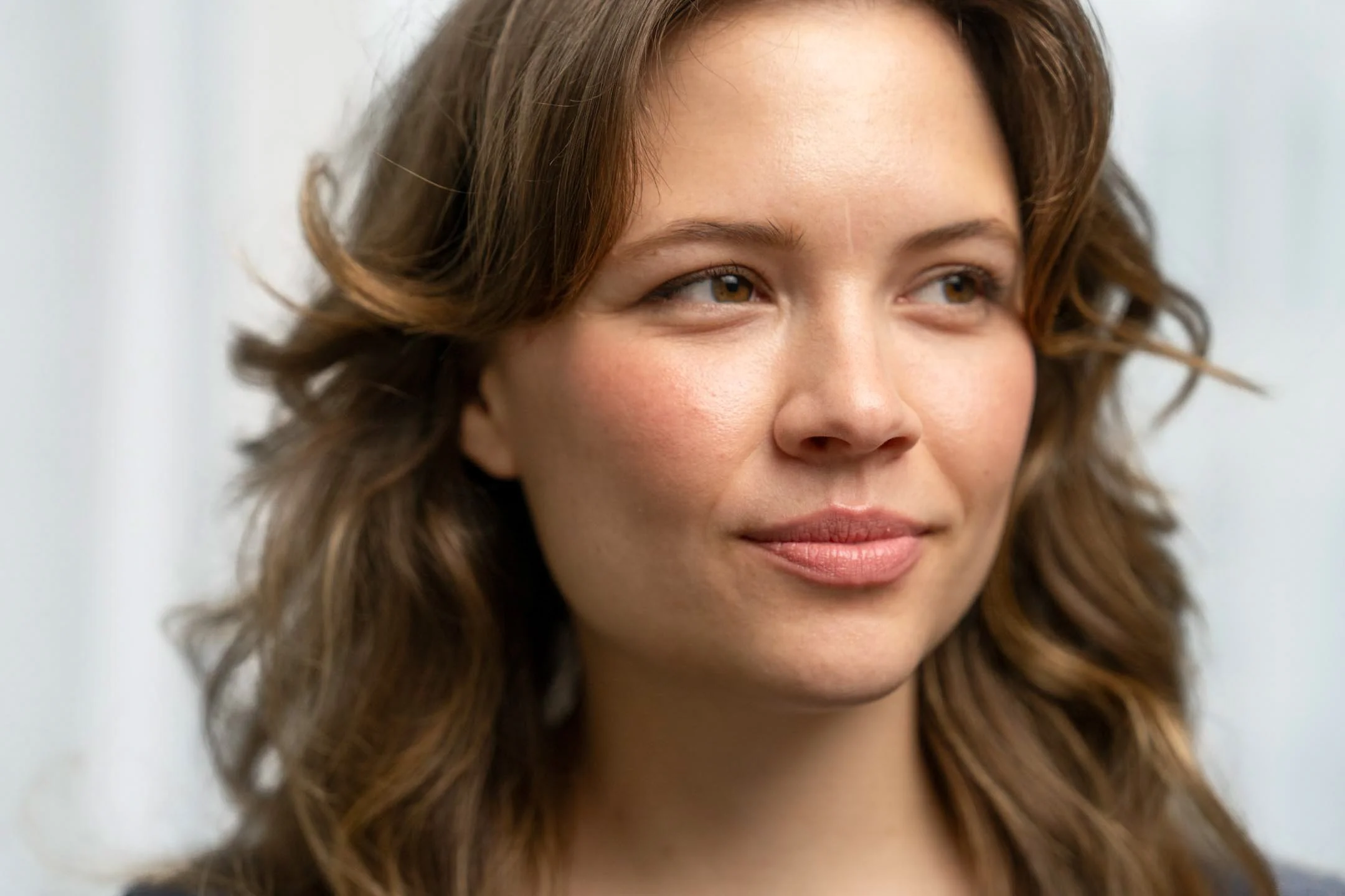 Close-up of a young woman with wavy brown hair and light makeup, smiling softly.