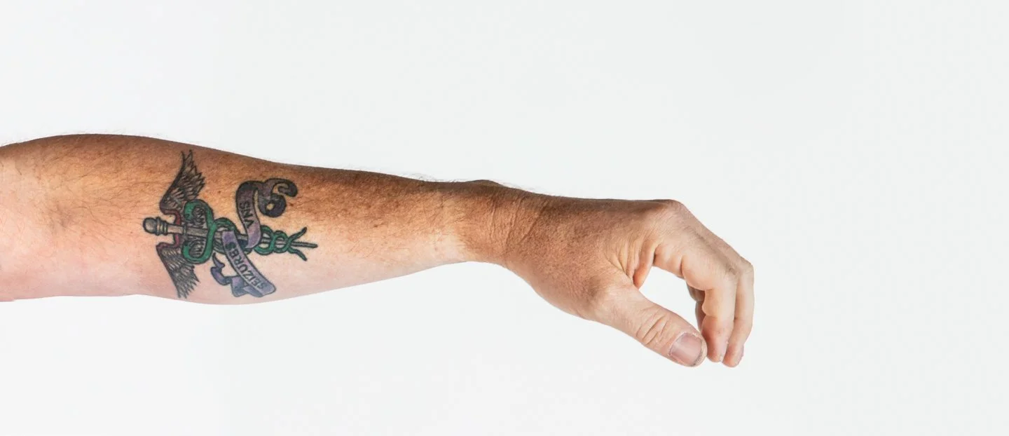 A person's arm with a tattoo of a snake and a dagger.