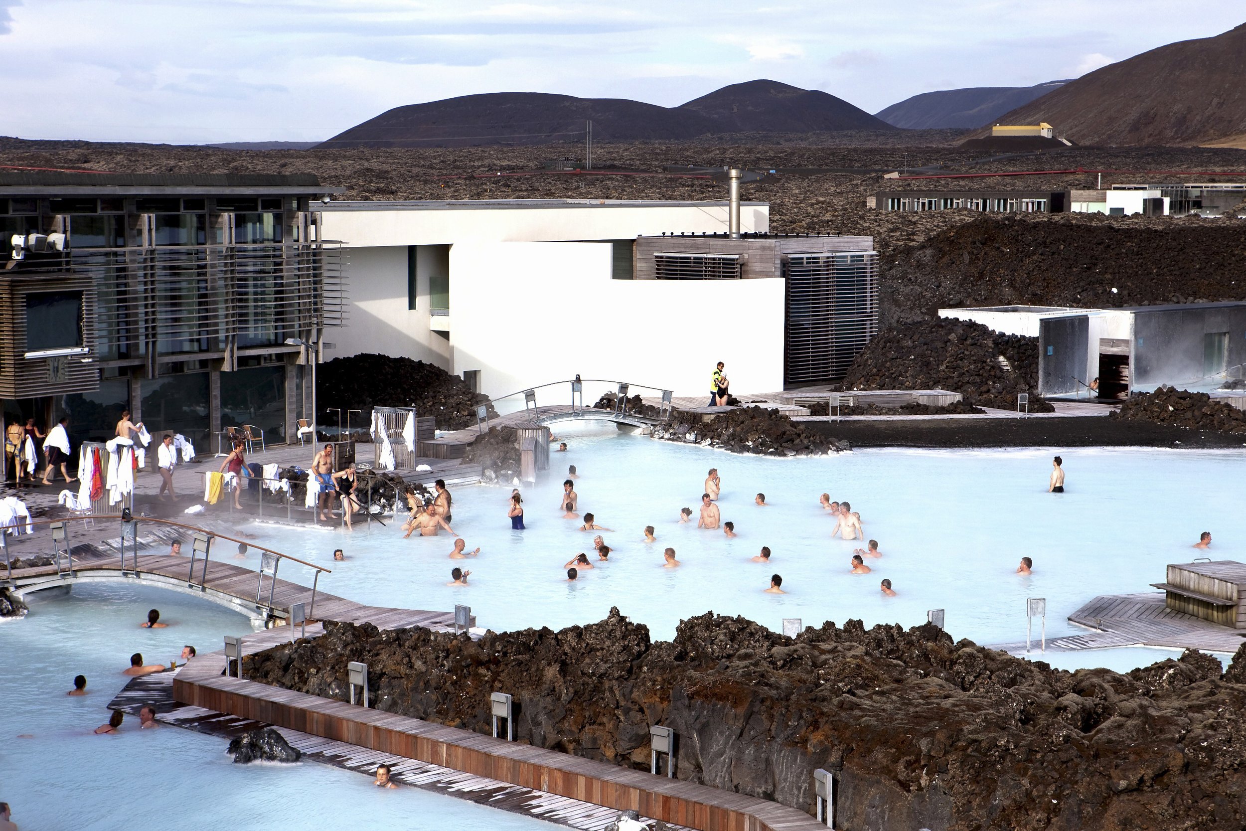 People enjoying a geothermal spa with steaming pools, surrounded by volcanic rock in a volcanic landscape.