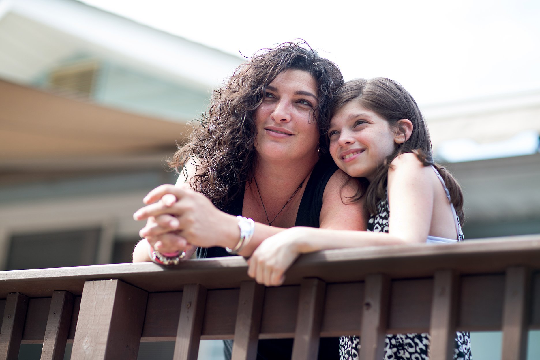 A woman and a girl leaning on a wooden railing, smiling and looking to the side.