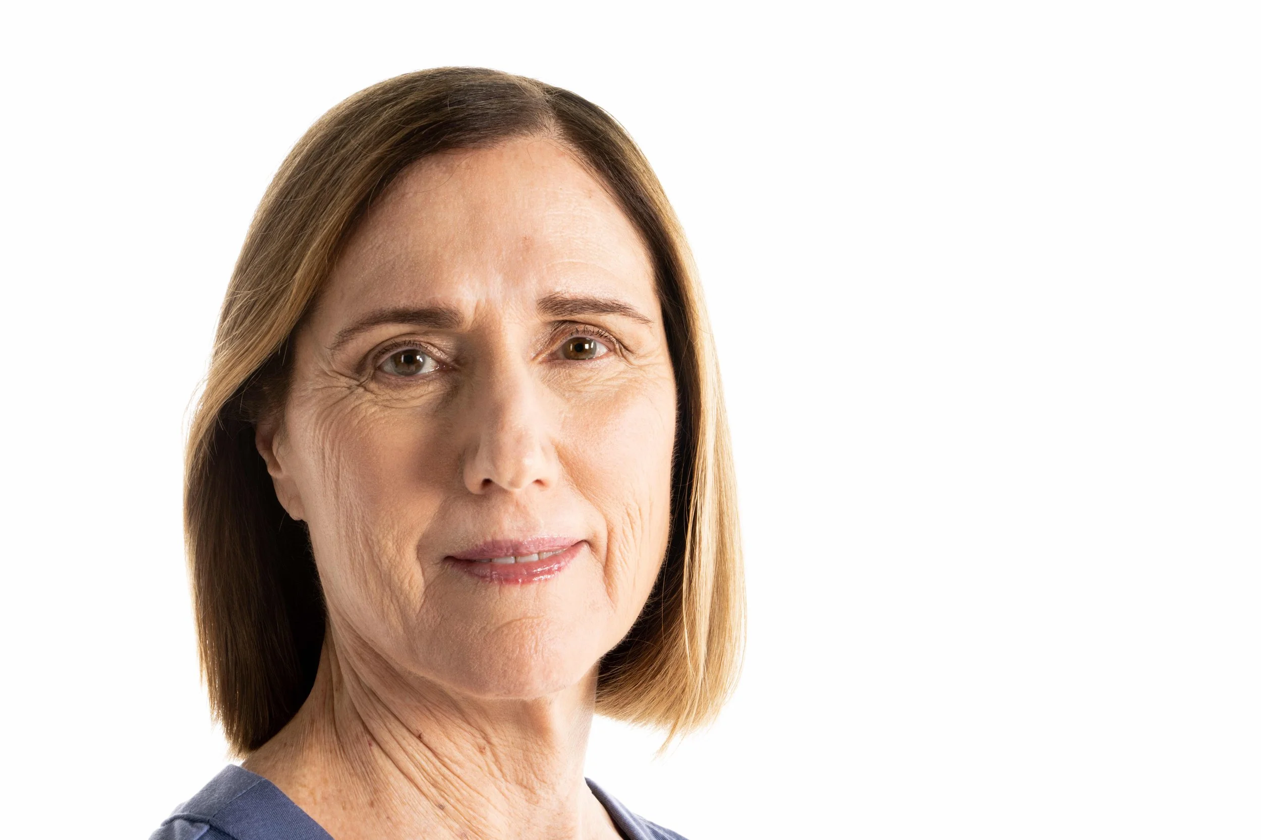 Close-up of a middle-aged woman with shoulder-length light brown hair, wearing a blue top, smiling slightly, against a plain white background.