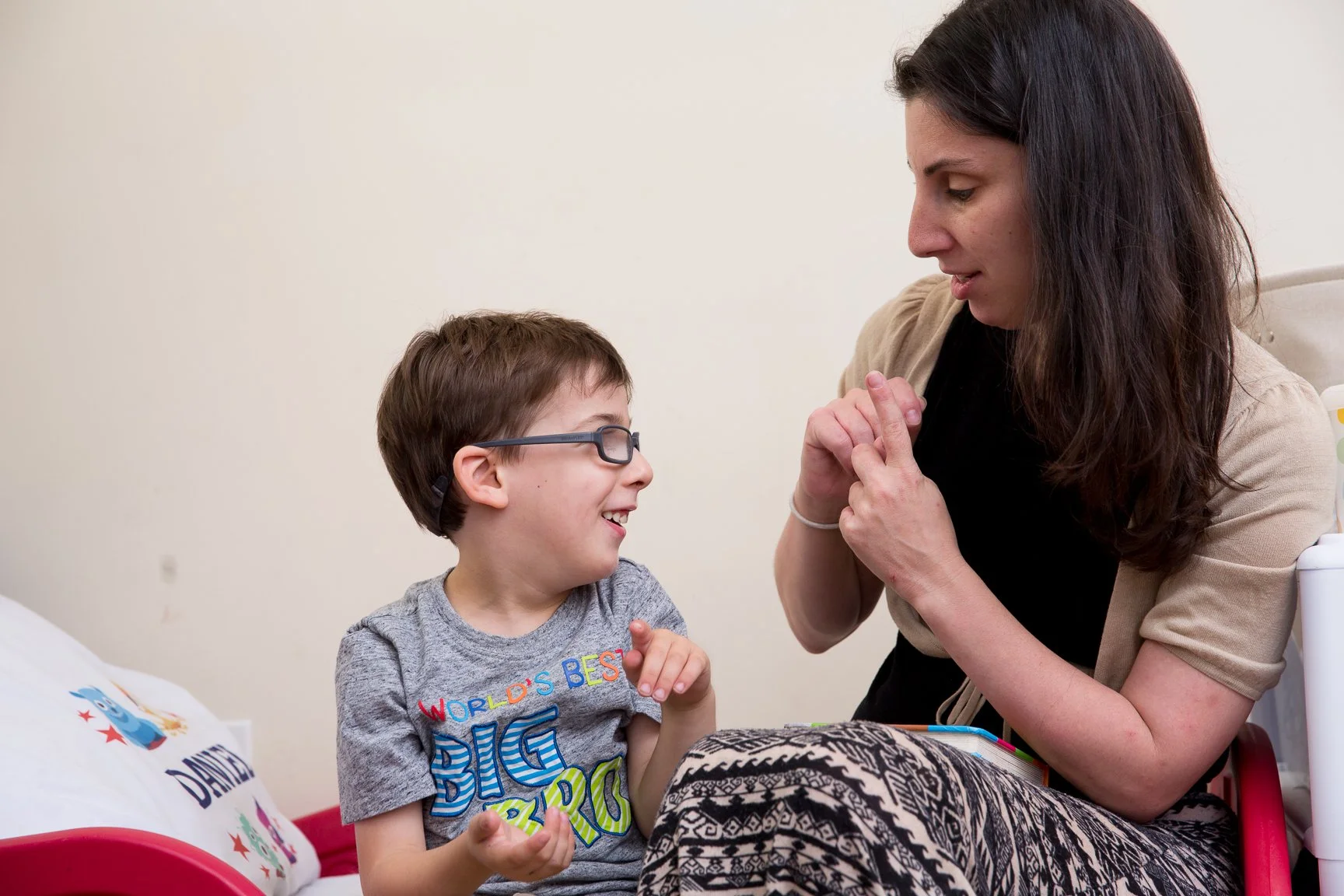A young boy with glasses and a mom sitting in a hospital room, smiling and engaging with each other.