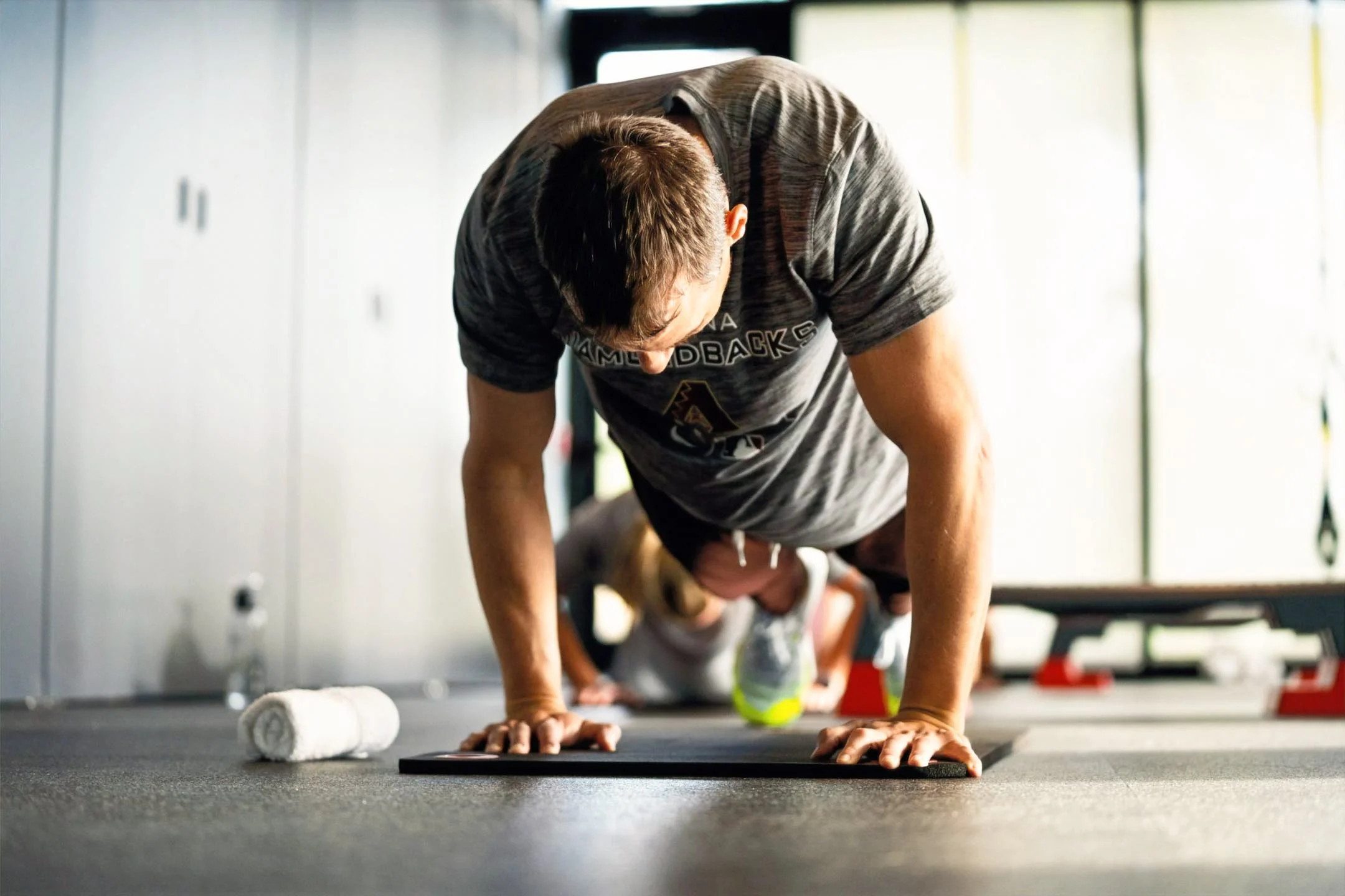 Man doing push-ups in a gym with equipment and a towel nearby.