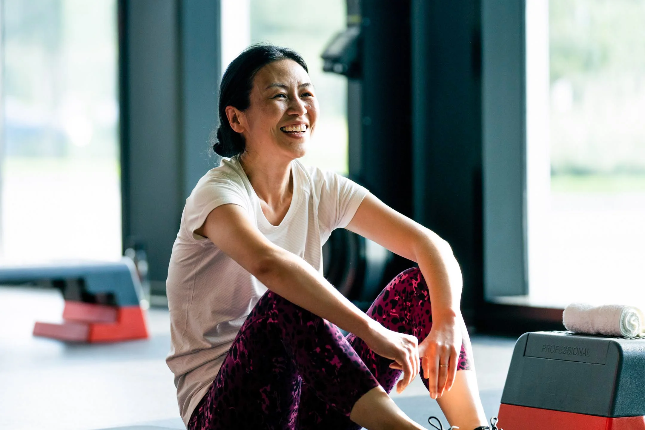 Woman smiling and sitting on the floor near workout equipment in a gym.