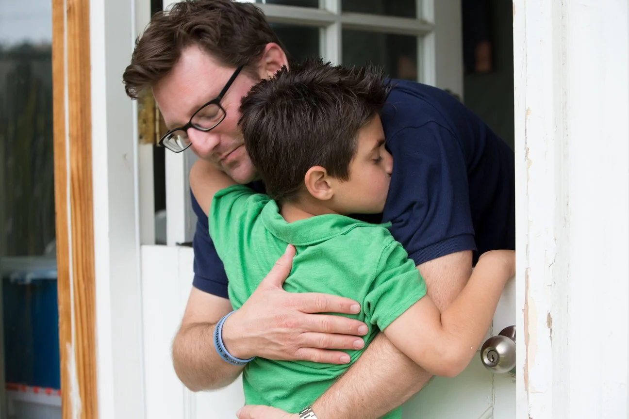 A man and two boys share a warm hug outside at the door of a house.