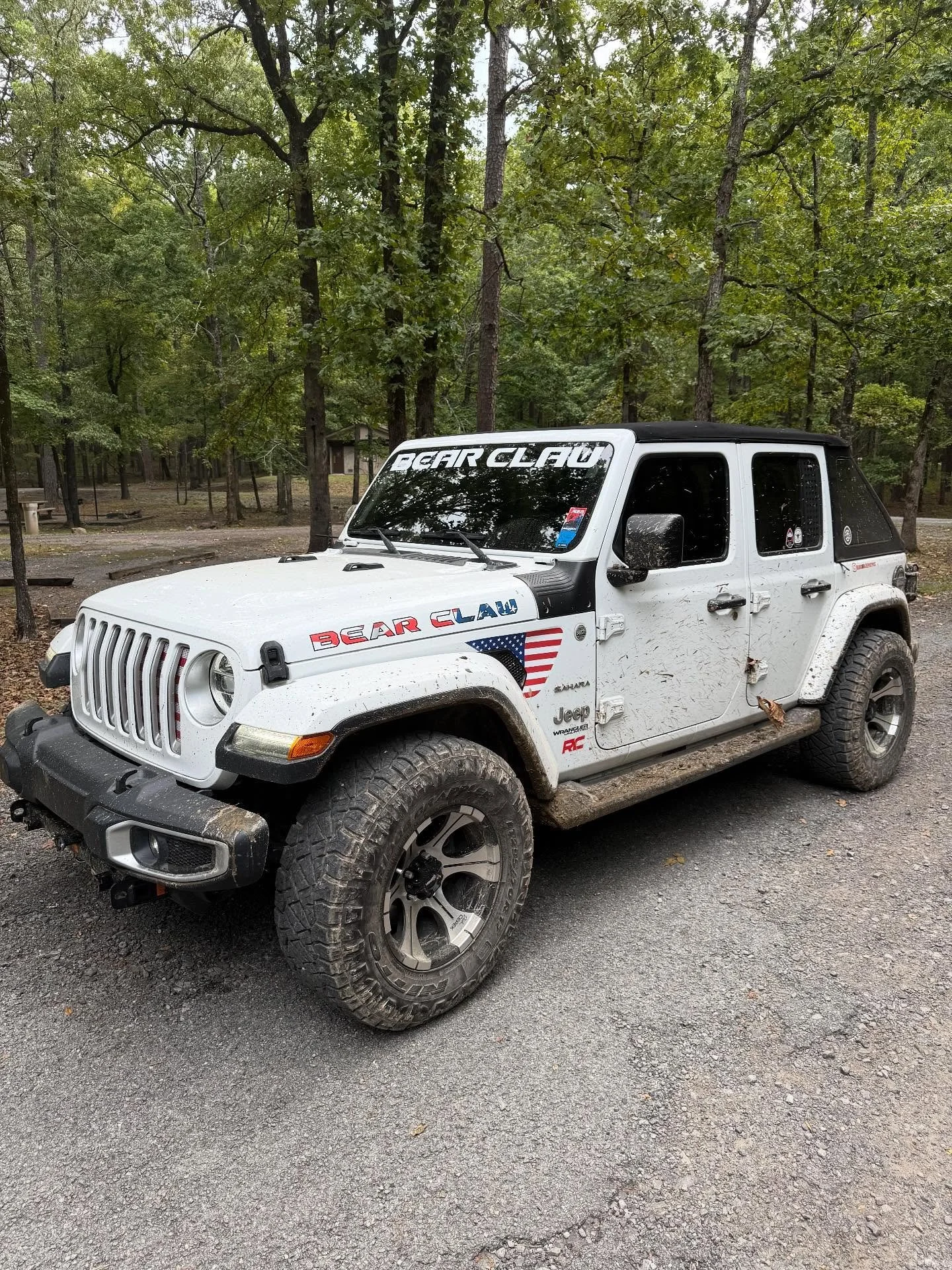 White Jeep with Bear Claw Stickers outdoors in woods after mudding