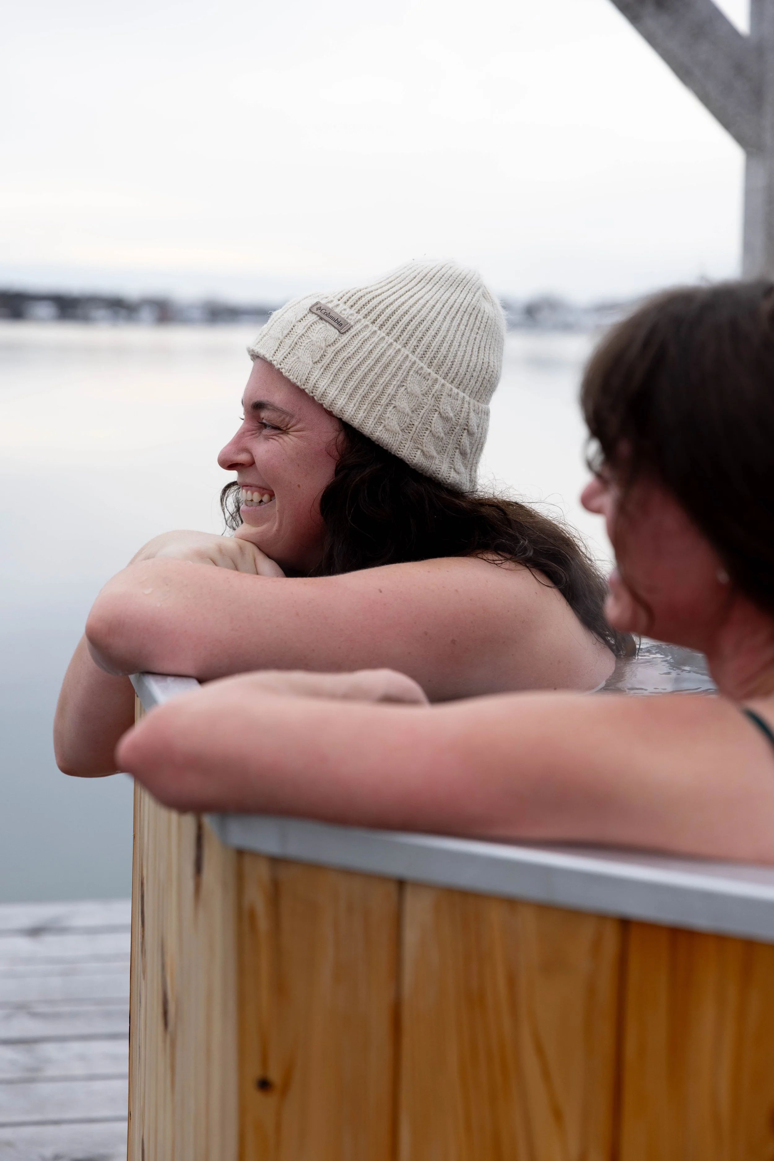 Woman smiling and relaxing in a wooden hot tub outdoors on a cloudy day.