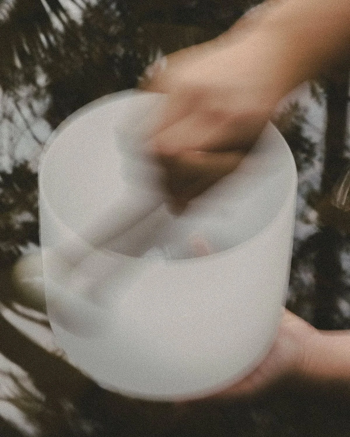 Close-up of a person's hand holding a white mug, with dark curly hair in the background.