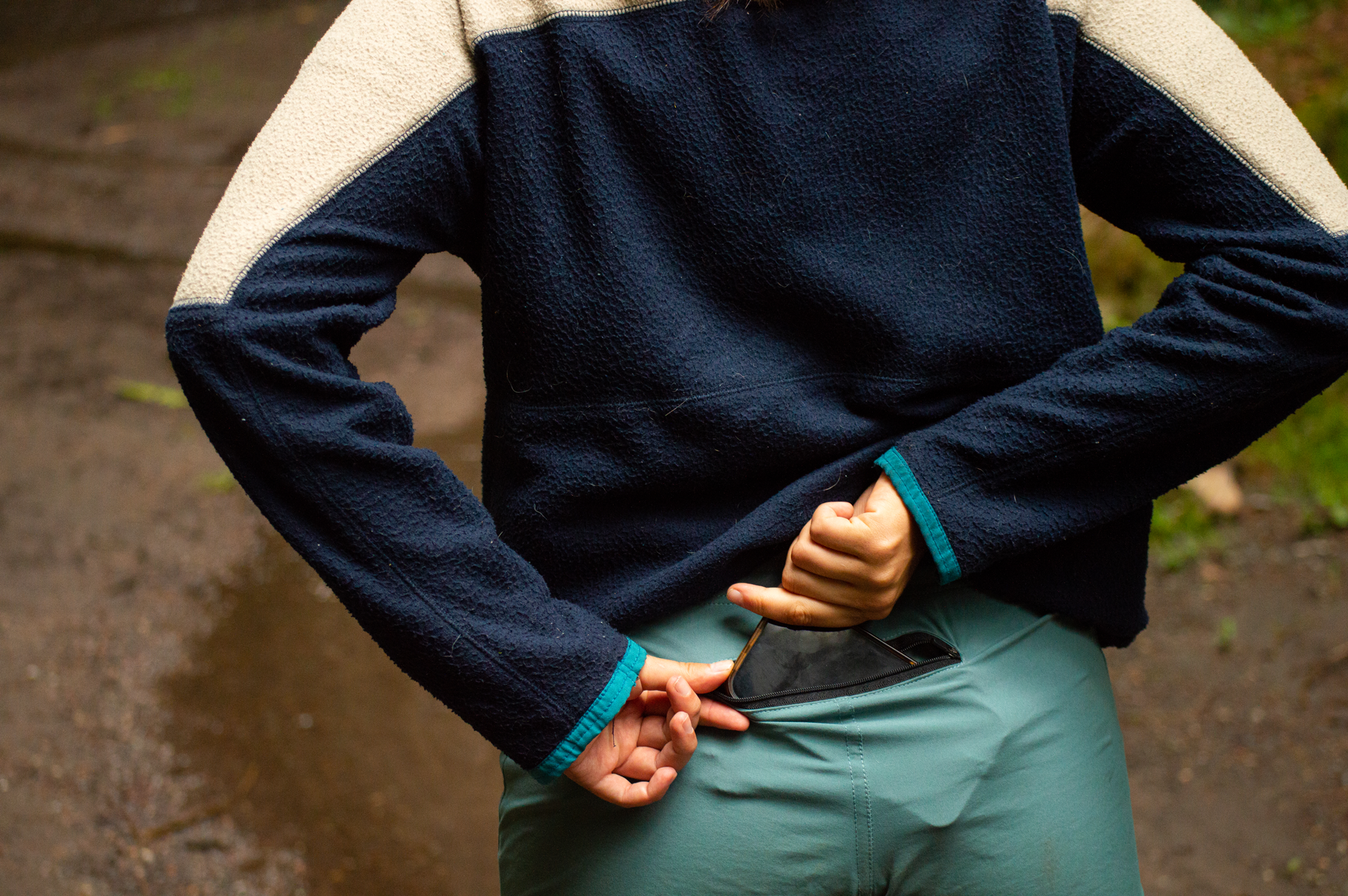 Person in outdoor clothing, pulling phone out of back pocket on trail.