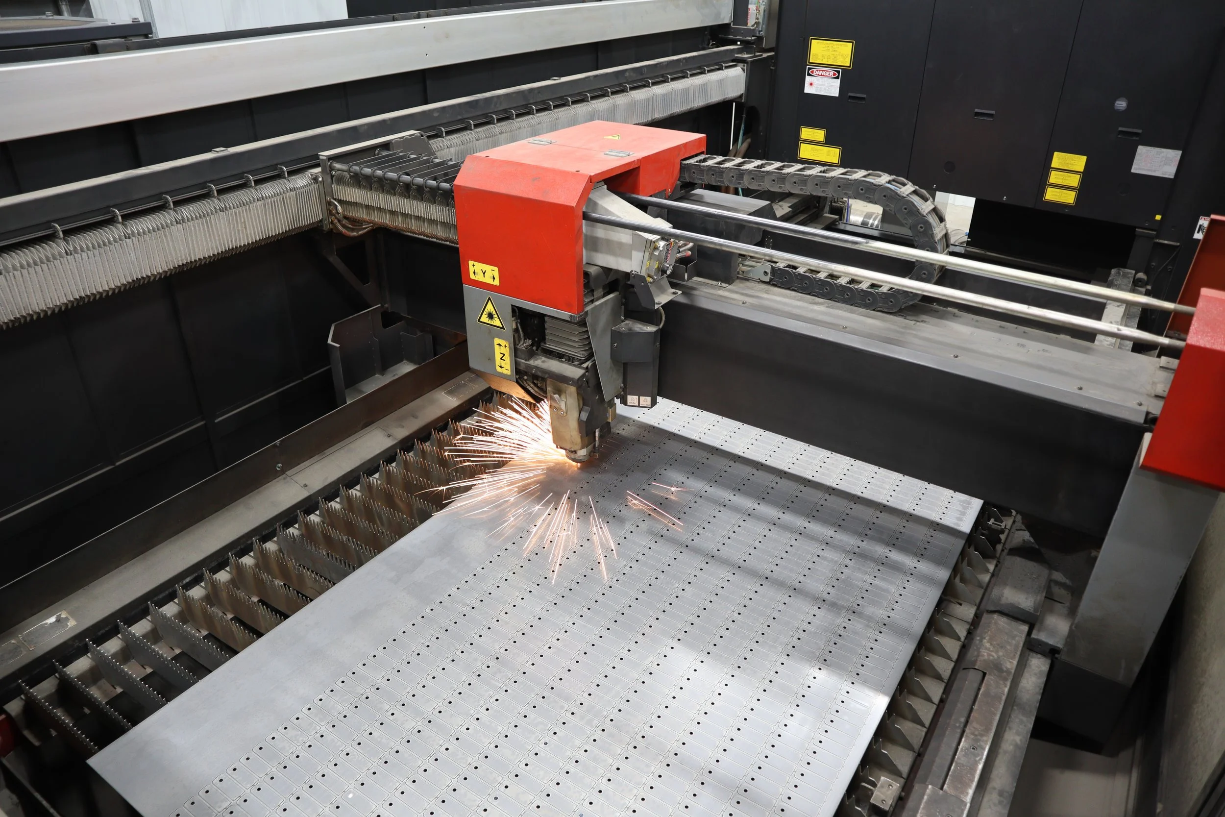 Laser cutting machine engraving metal sheet, sparks flying, industrial manufacturing setting.