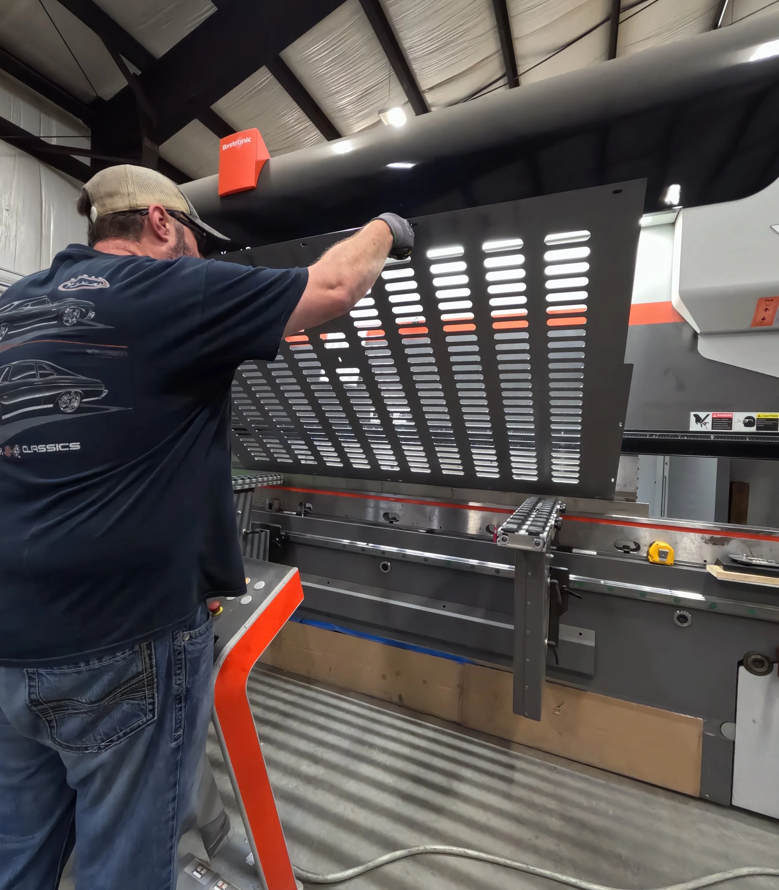 A worker is operating a hydrographic film printer, applying a black and white striped pattern to a car part in an industrial facility.