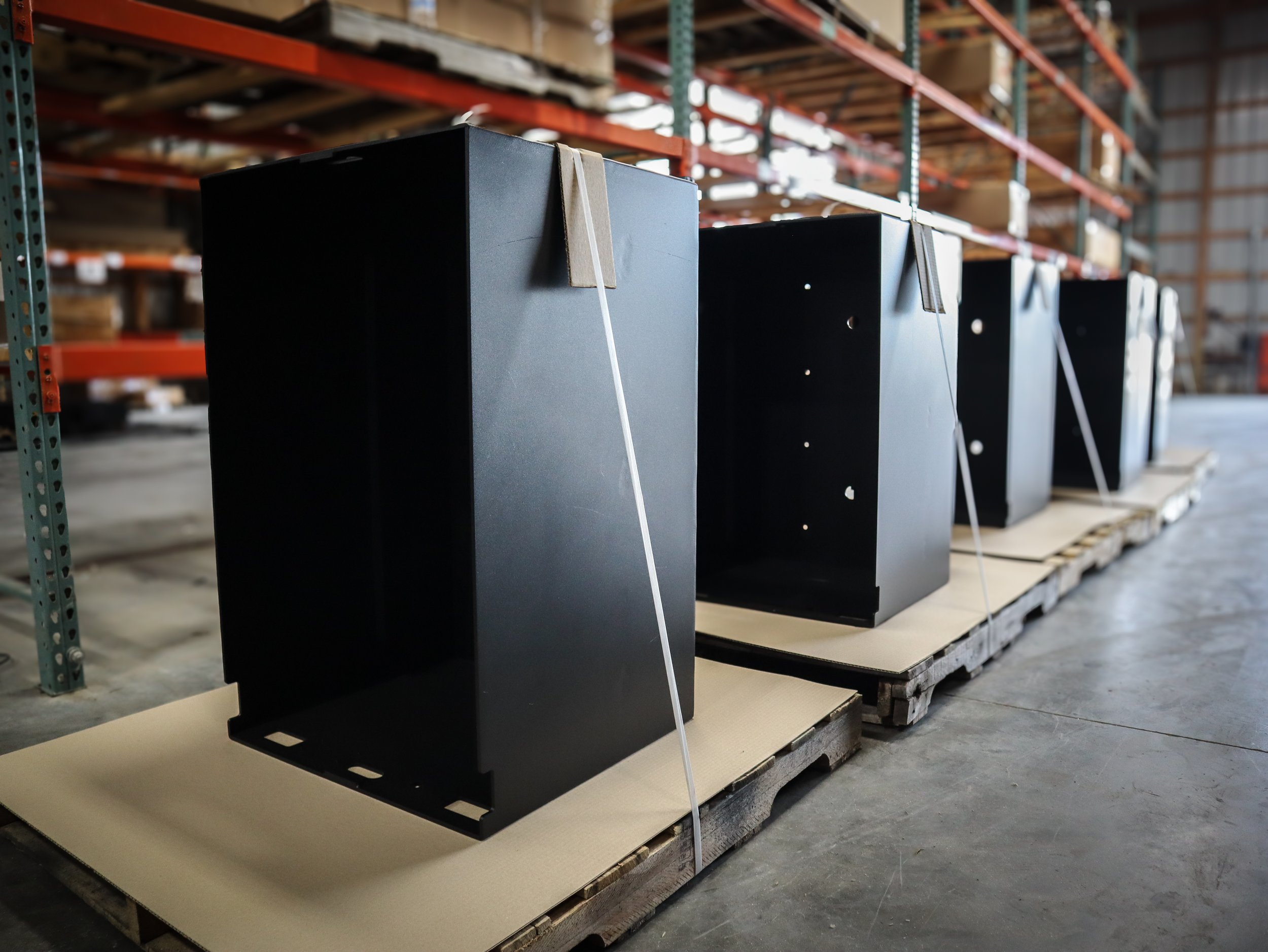 Four powder coated metal parts assembled and secured on pallets in a warehouse.