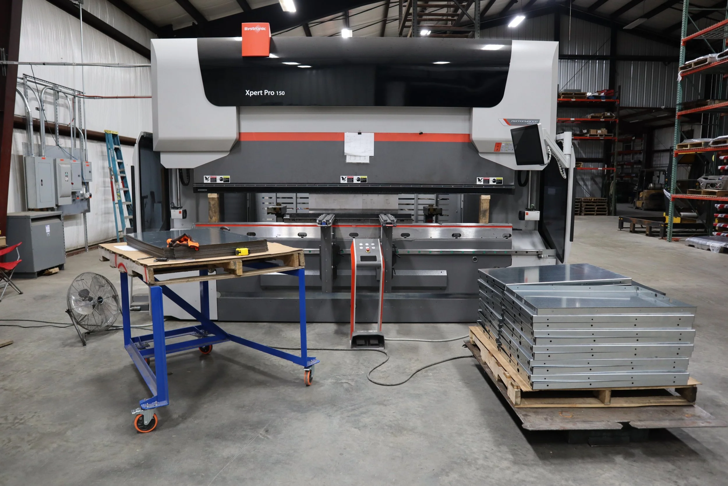 Industrial manufacturing metal forming machine in a facility and metal parts on a pallet, and various tools and equipment around.