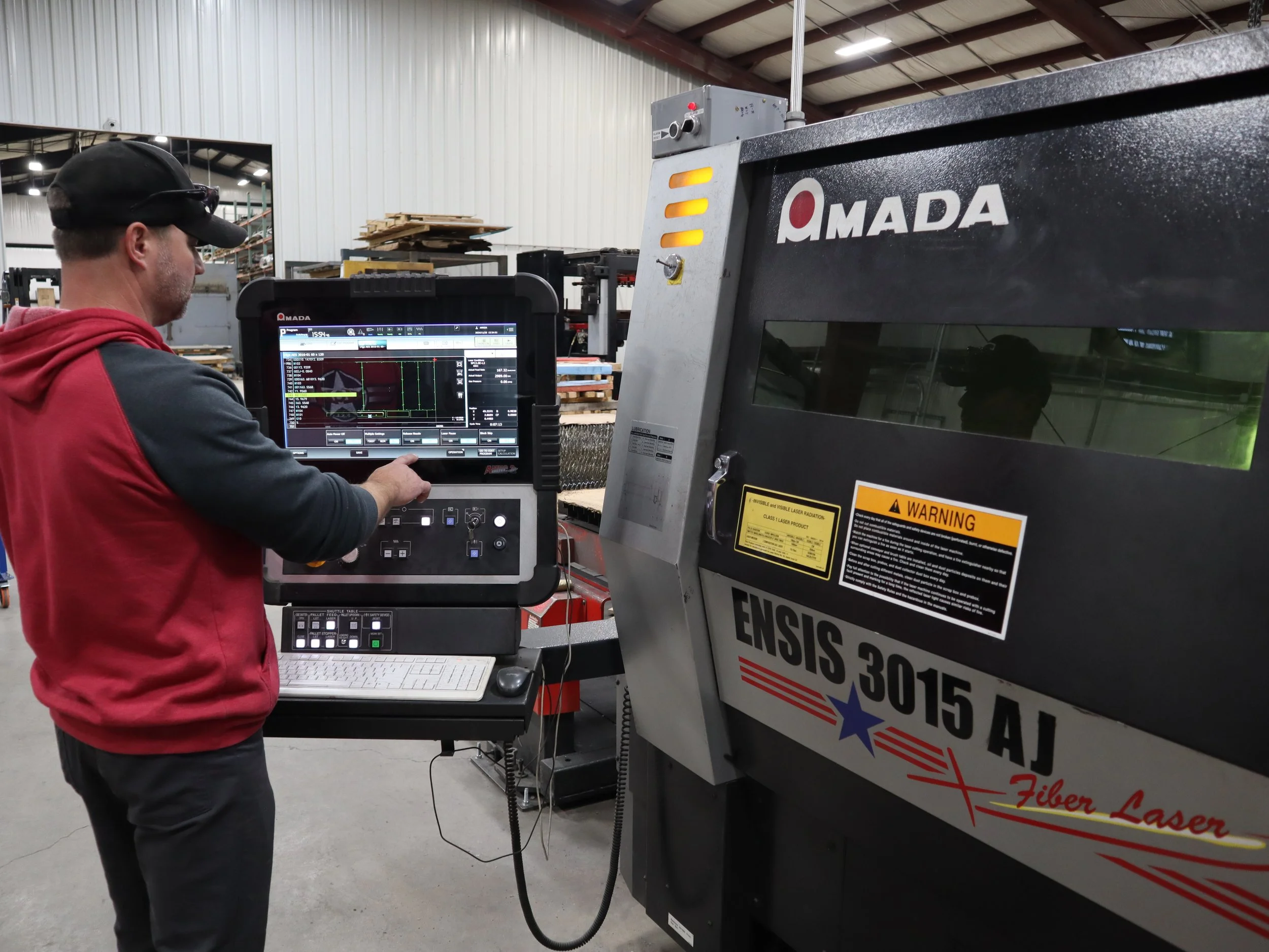 A man in a red and black hoodie operating a laser cutting machine in a factory.