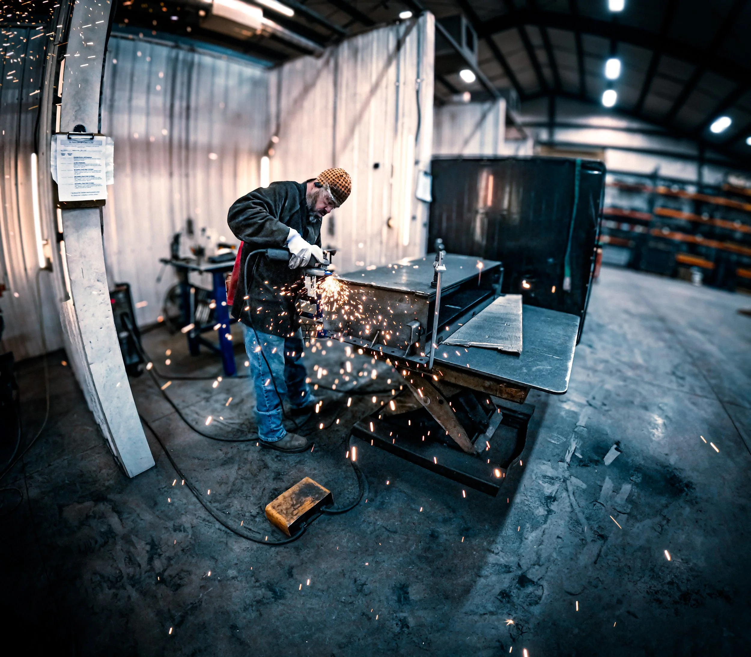 A man welding metal in a workshop, sparks flying around as he uses a welding tool.