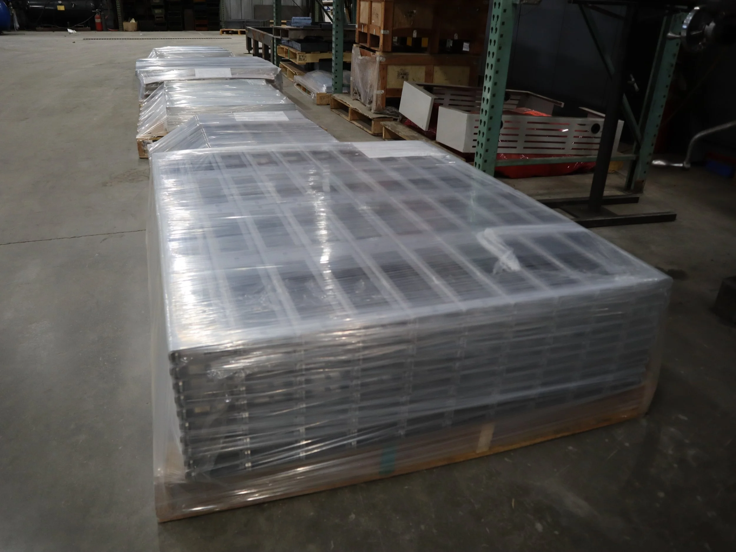 Large stack of metal shelves wrapped in plastic in a warehouse, with storage racks and pallets in the background.