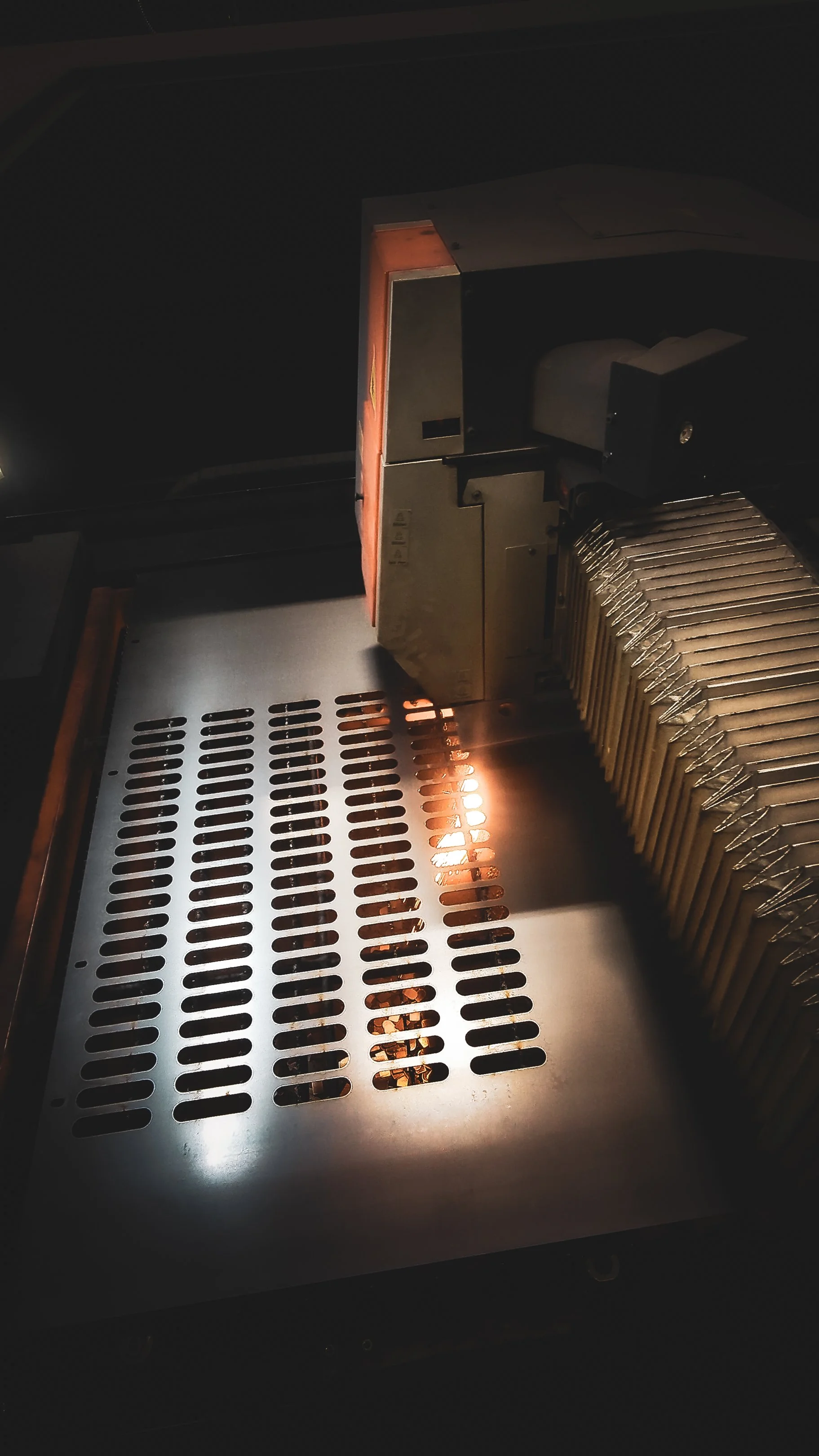 Close-up of a laser cutting machine with a bright laser beam cutting through a metal sheet, creating sparks.