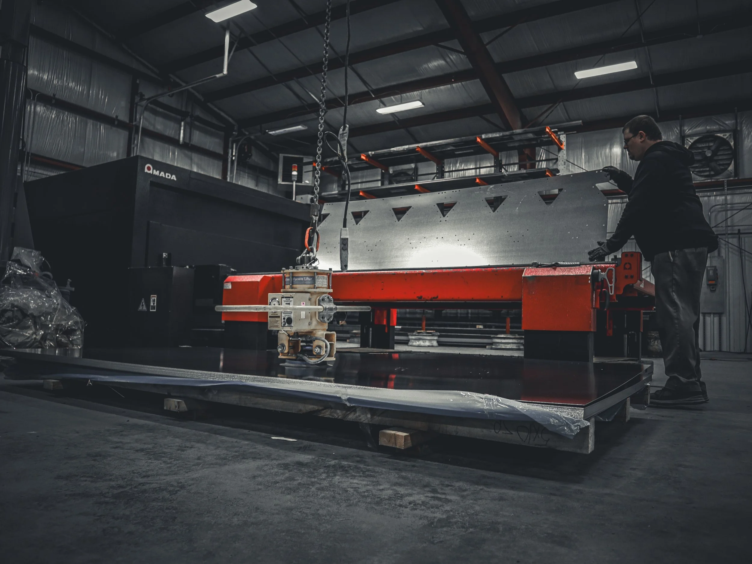A person working with a large industrial machine in a warehouse or factory setting, with metal surfaces and equipment surrounding them.