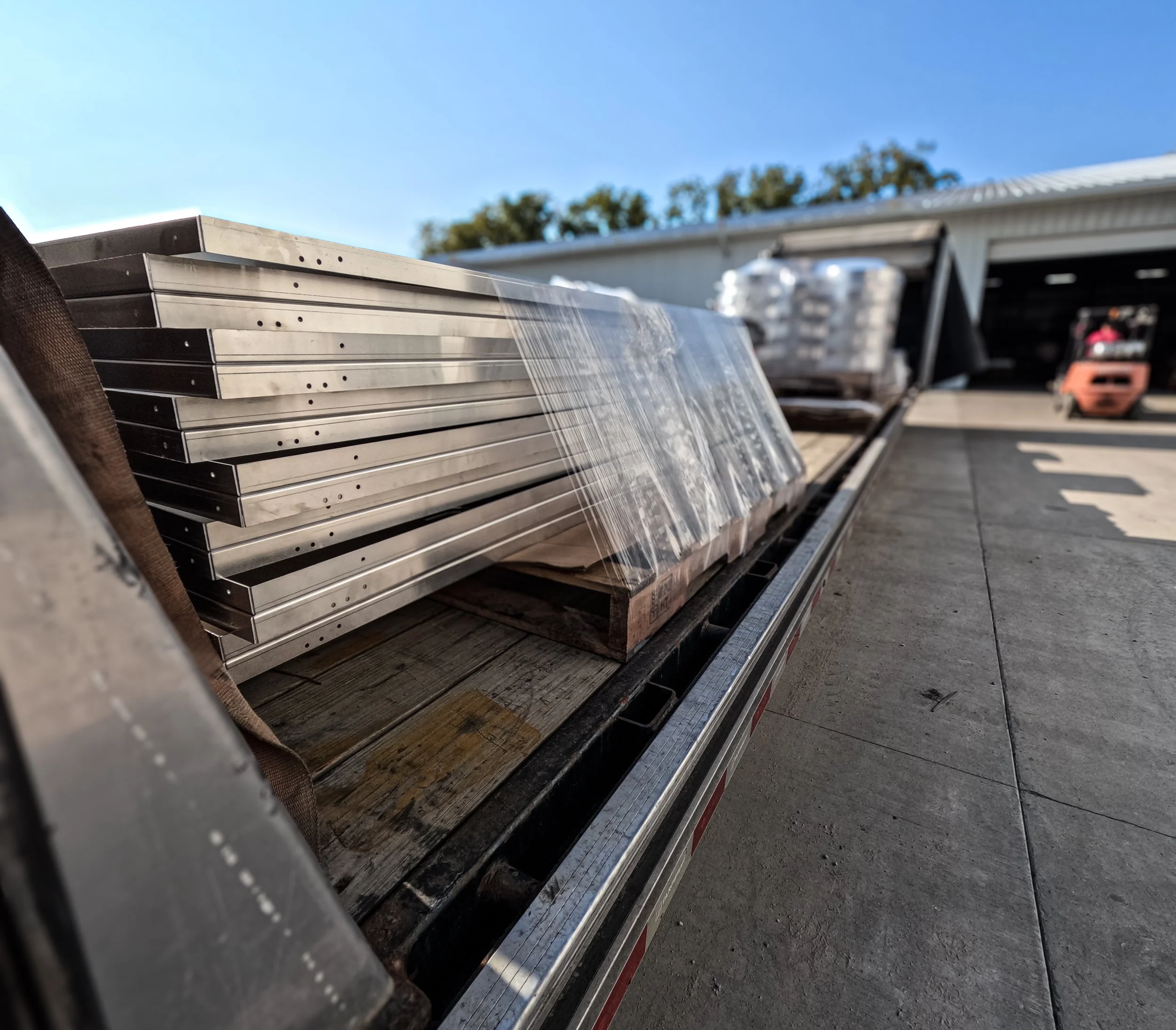 Metal beams on a flatbed truck with water flowing over them under clear blue sky.