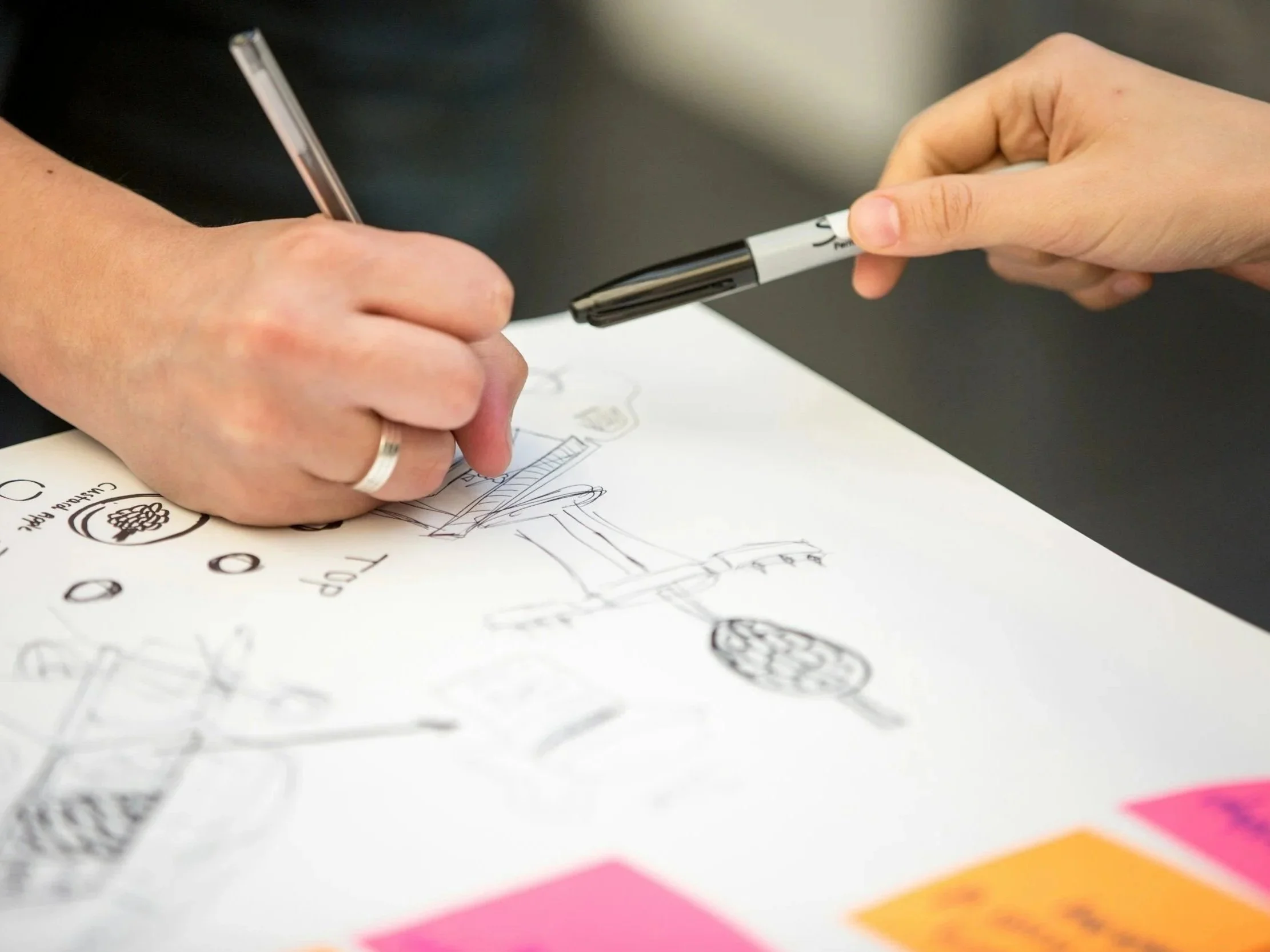 Person drawing sketches and notes on a white sheet of paper with markers.