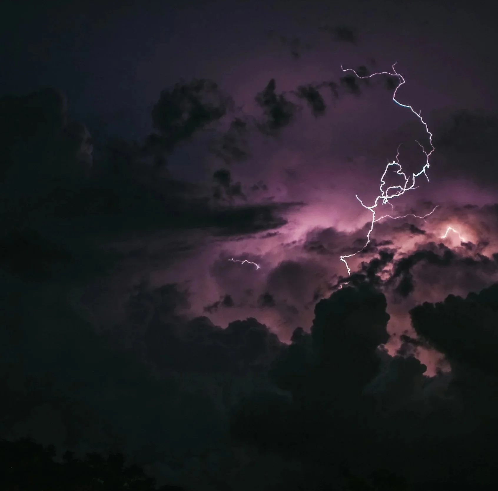 Night sky with dark clouds and visible lightning bolts illuminating purple-tinged clouds.