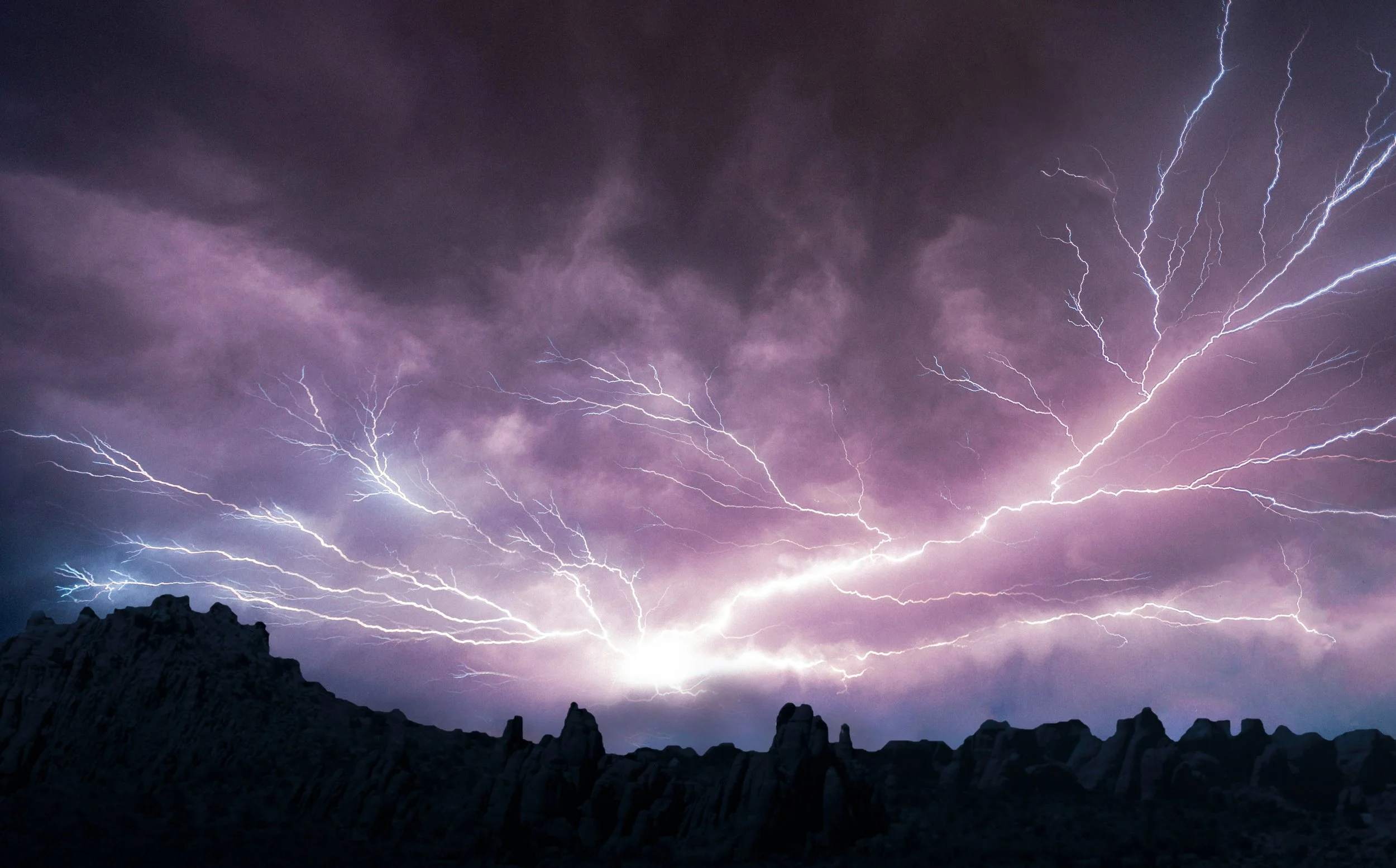 Lightning storm over a mountain range at night with dark clouds and multiple lightning bolts.