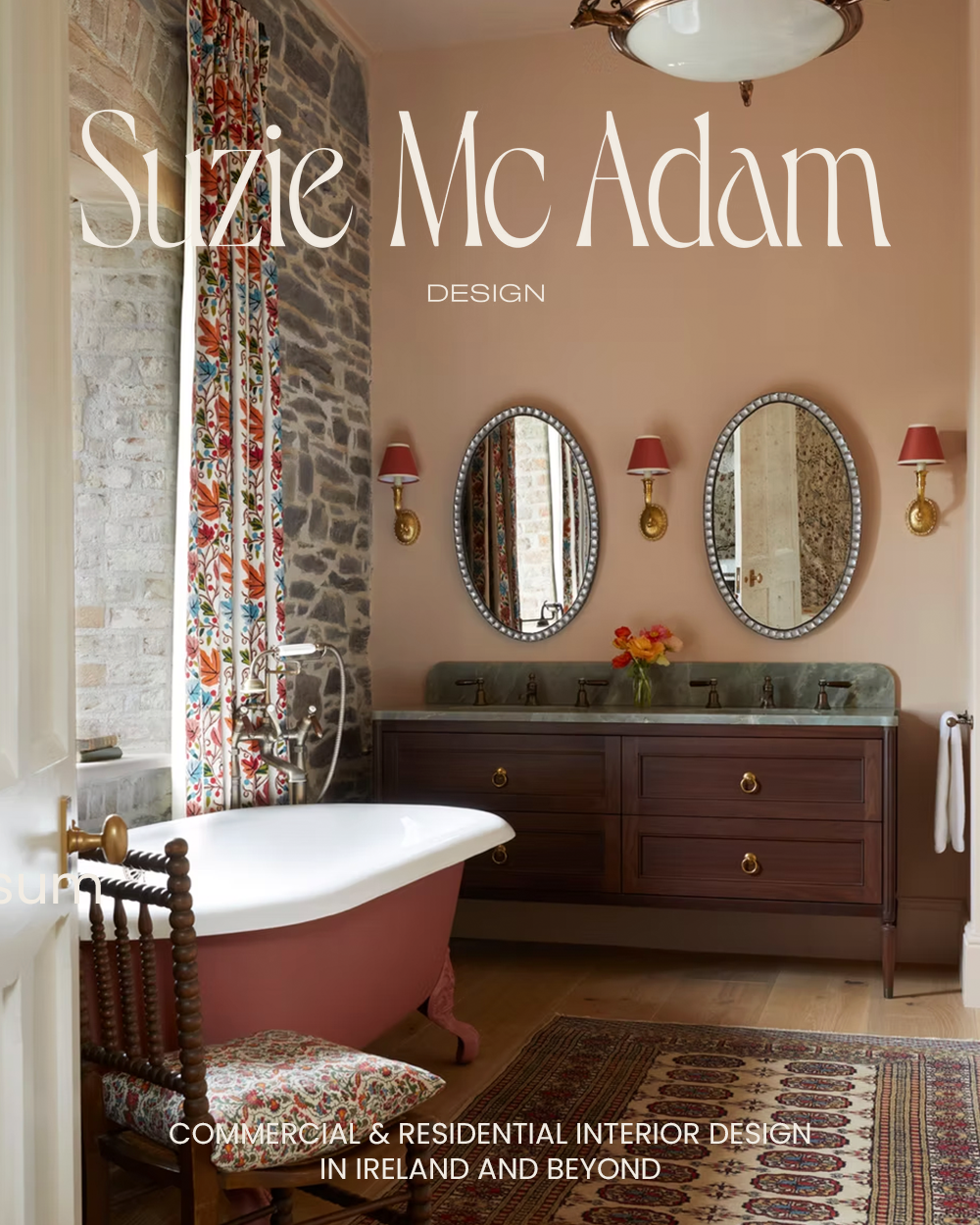 Interior of a vintage-style bathroom featuring a pink clawfoot bathtub with a floral cushioned seat, a wooden vanity with double sinks, two oval mirrors, pink and brass wall sconces, a patterned curtain, a vase of flowers, a rug, and exposed brick wall elements.