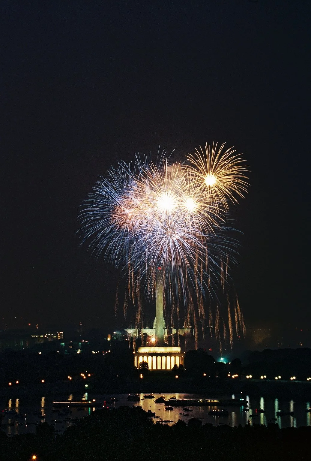Fireworks display over the Washington Monument at night, with reflections in the water below.