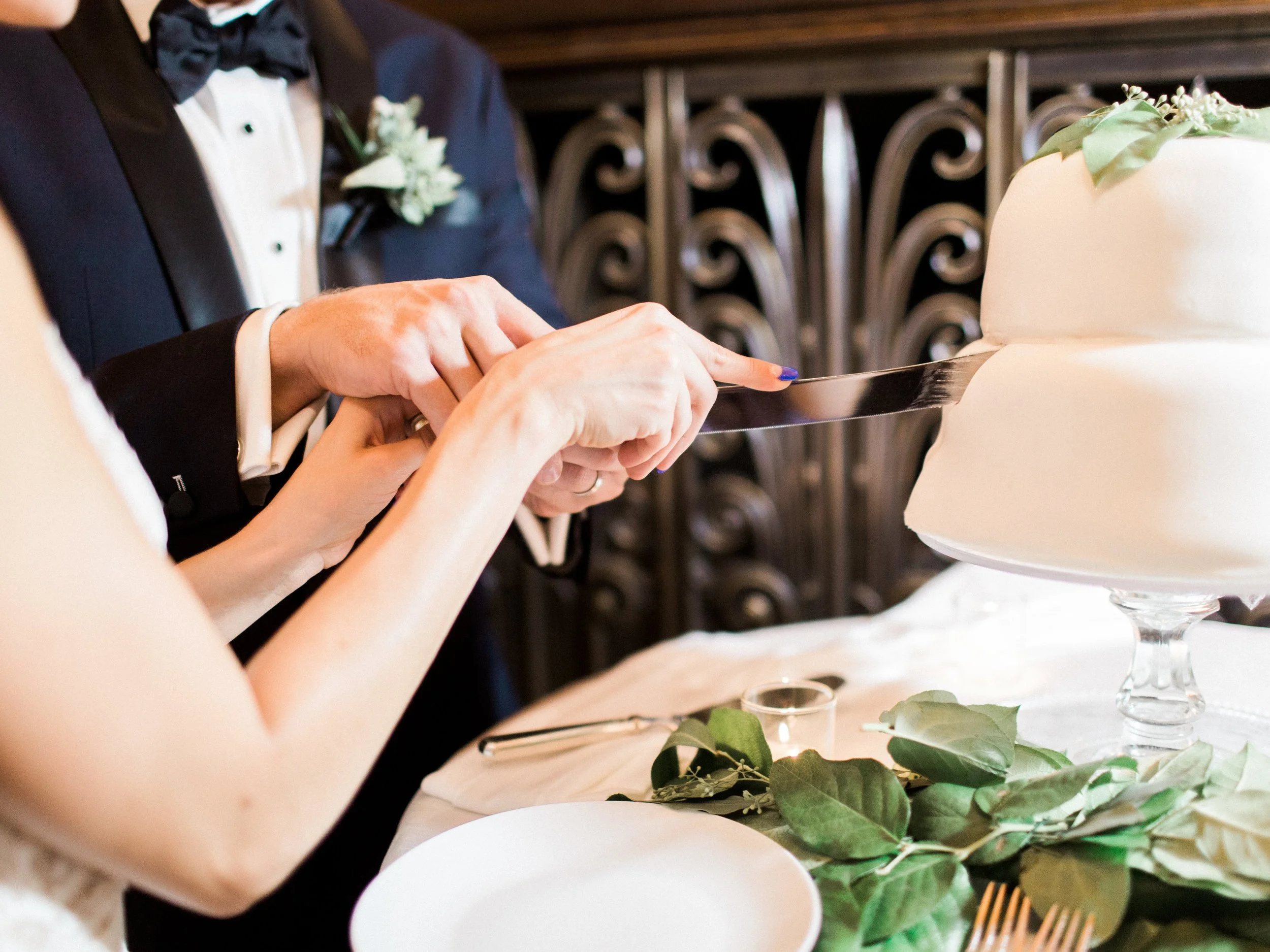 A couple in wedding attire cutting a white wedding cake with a knife at their wedding reception.
