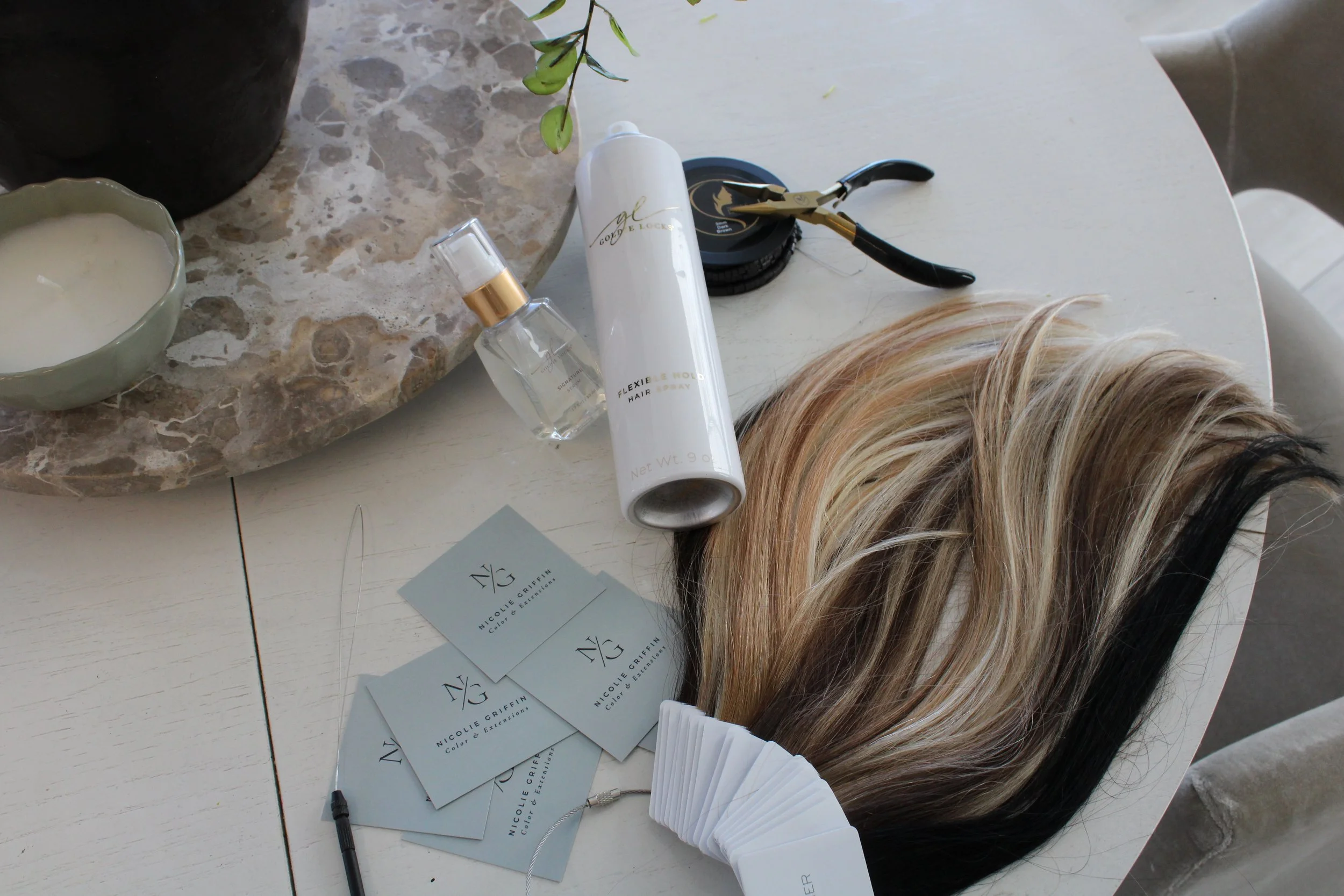 A round white table with various hair coloring and styling items, including a wig, hair spray, business cards, and a candle.