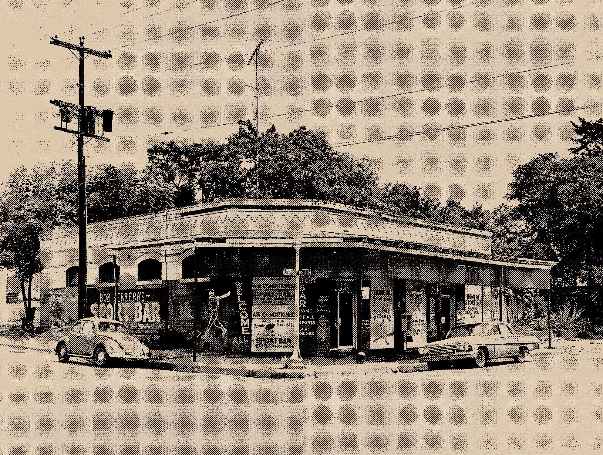 A vintage corner building with signs advertising a sport bar, smoking, and lottery services, surrounded by parked cars and trees, with power lines overhead.