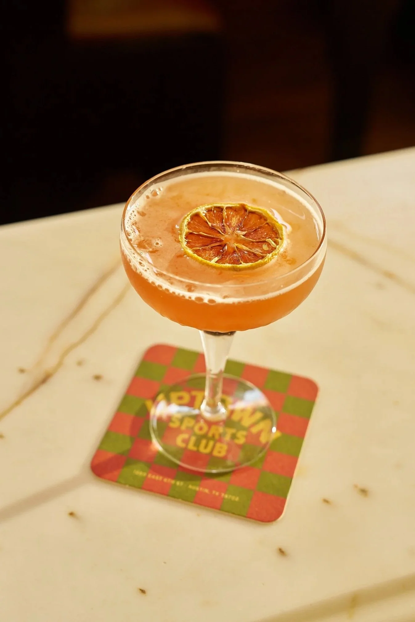 A pink marble cocktail with a dried lemon slice on top, placed on a colorful checkered coaster. Uptown’s cocktails, like the martini, negroni, old-fashioned and gimlet are craft cocktails at one of the best bars in Austin for locals and visitors.