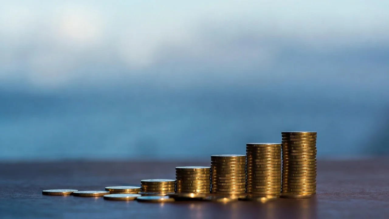 Stacked coins arranged in ascending order with a blurred blue sky background.