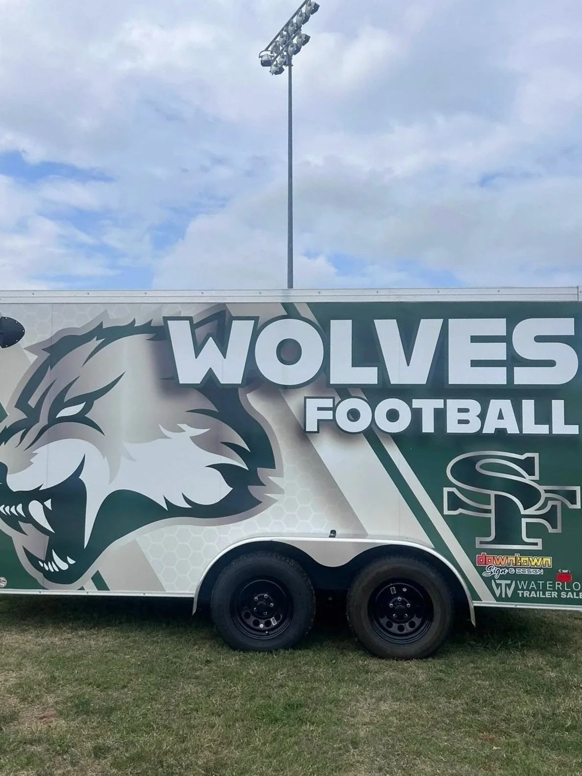 A football trailer with a wolf mascot and the words 'Wolves Football' parked on a grassy field under a cloudy sky. for edmond santa fe high school.