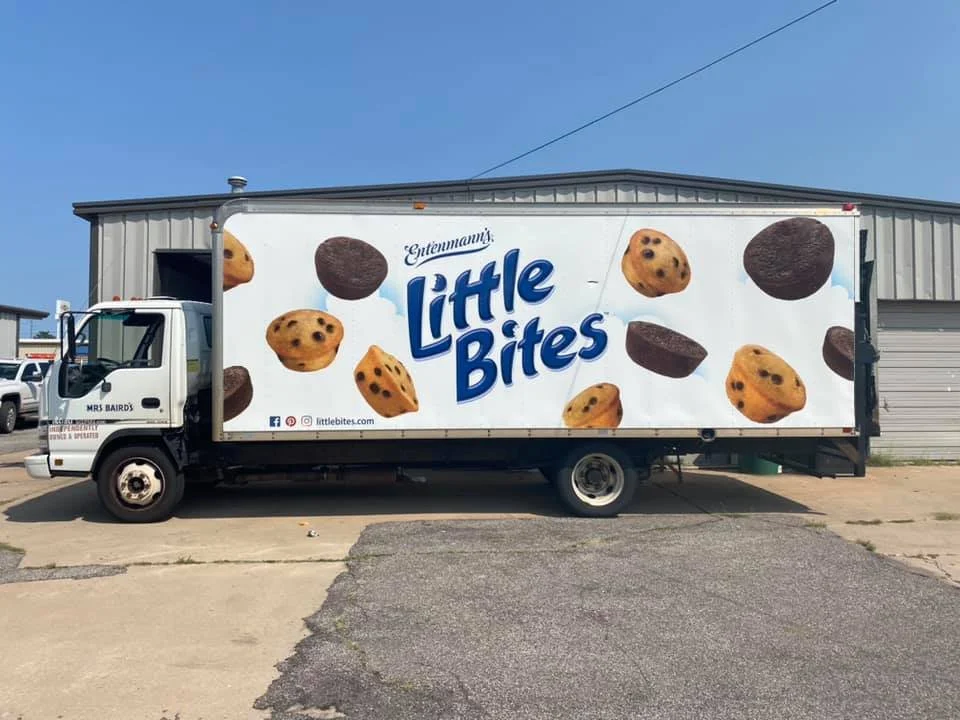 A truck with a large advertisement for Little Bites cookies featuring images of cookies, with the brand name in large blue letters across the middle.