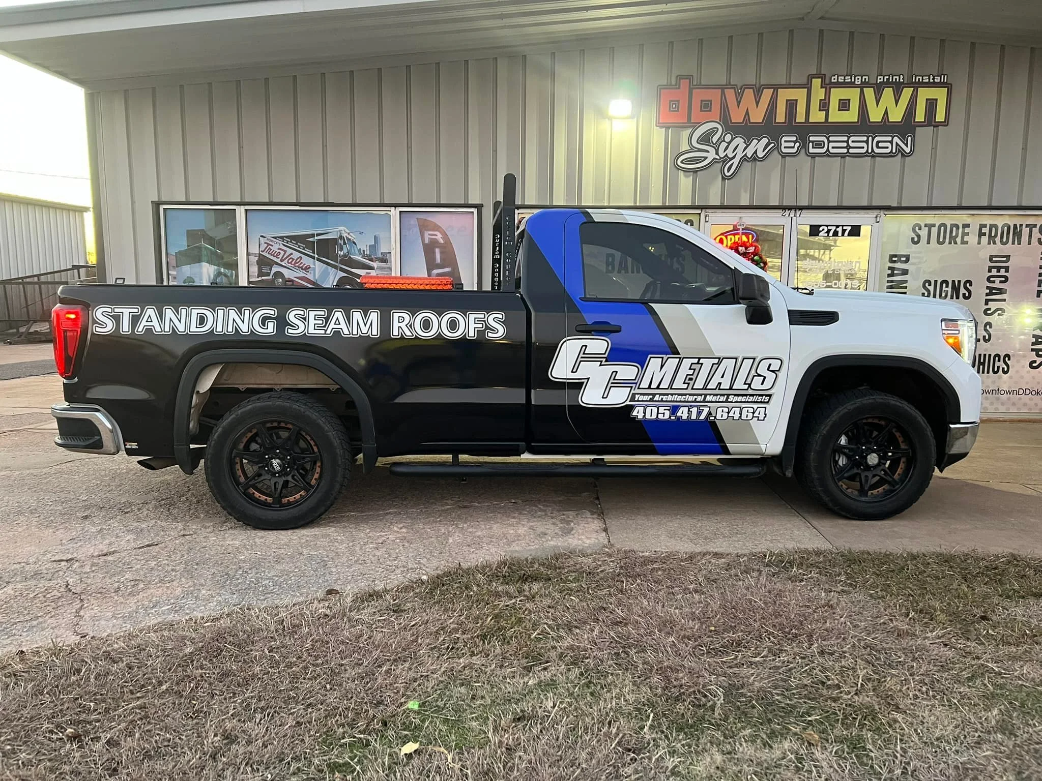 CC Metals standing seam roofs vehicle advertisement sign wrap blue grey and white on a truck in front of downtown sign and design