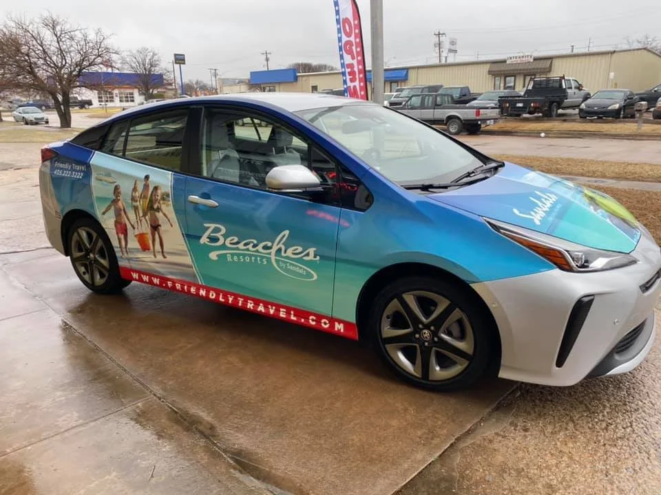 A blue and silver car with promotional ads for Beaches Resorts, featuring beach scene images and text on the side. The car is parked on a wet concrete surface.